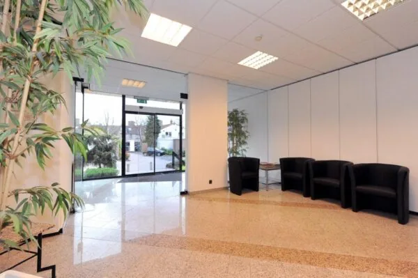 Modern office lobby at Oosteinde with black chairs, large indoor plants, and glass entrance doors.