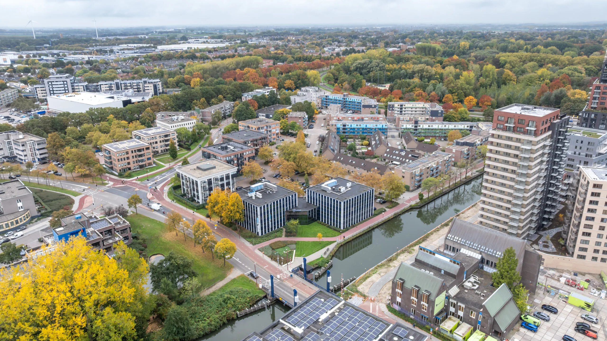Aerial view of the Krijtwal area featuring modern office buildings, residential apartments, canals, and autumn-colored trees in a suburban setting.