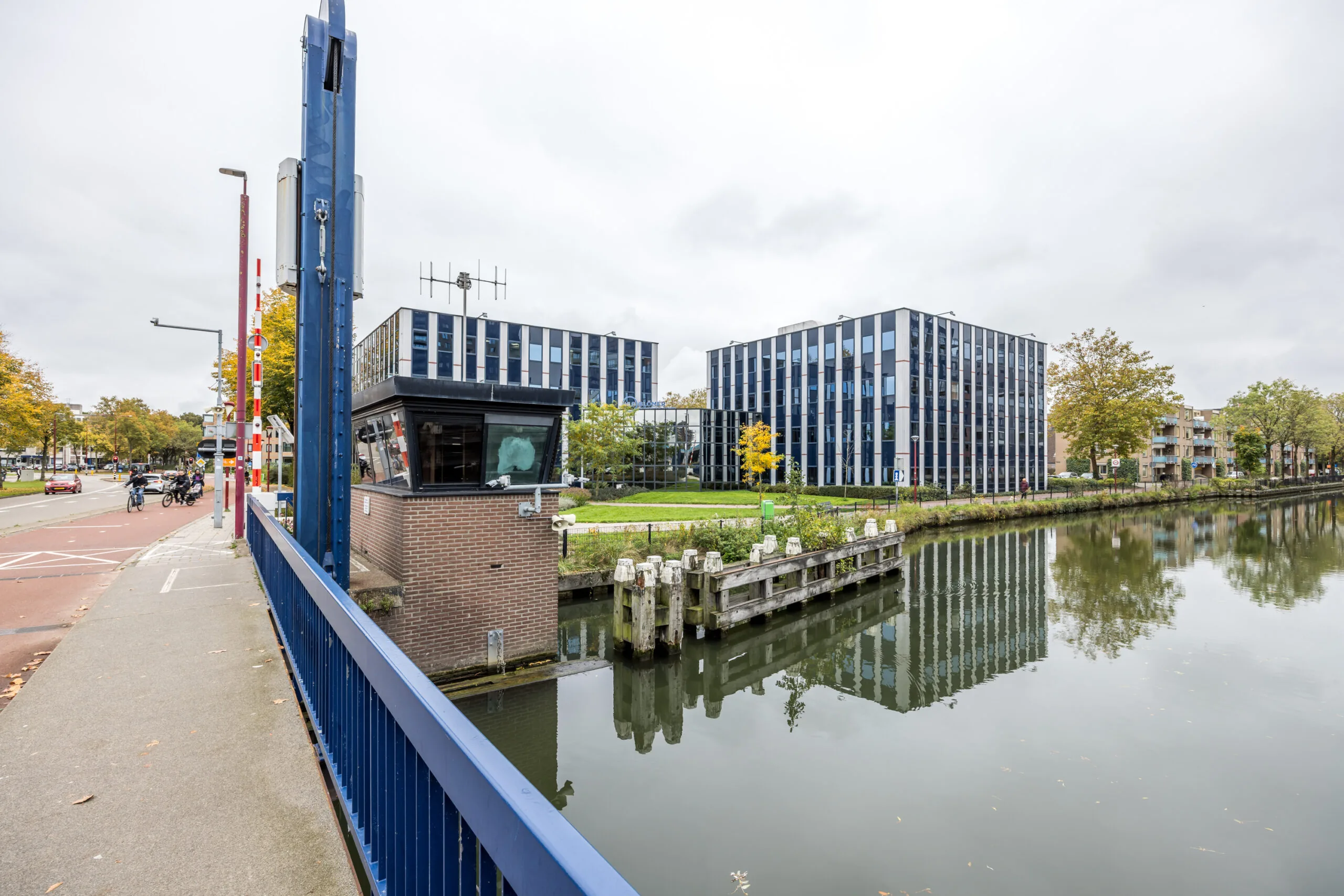 Modern office buildings on Krijtwal street reflected in a canal next to a blue drawbridge and control tower.