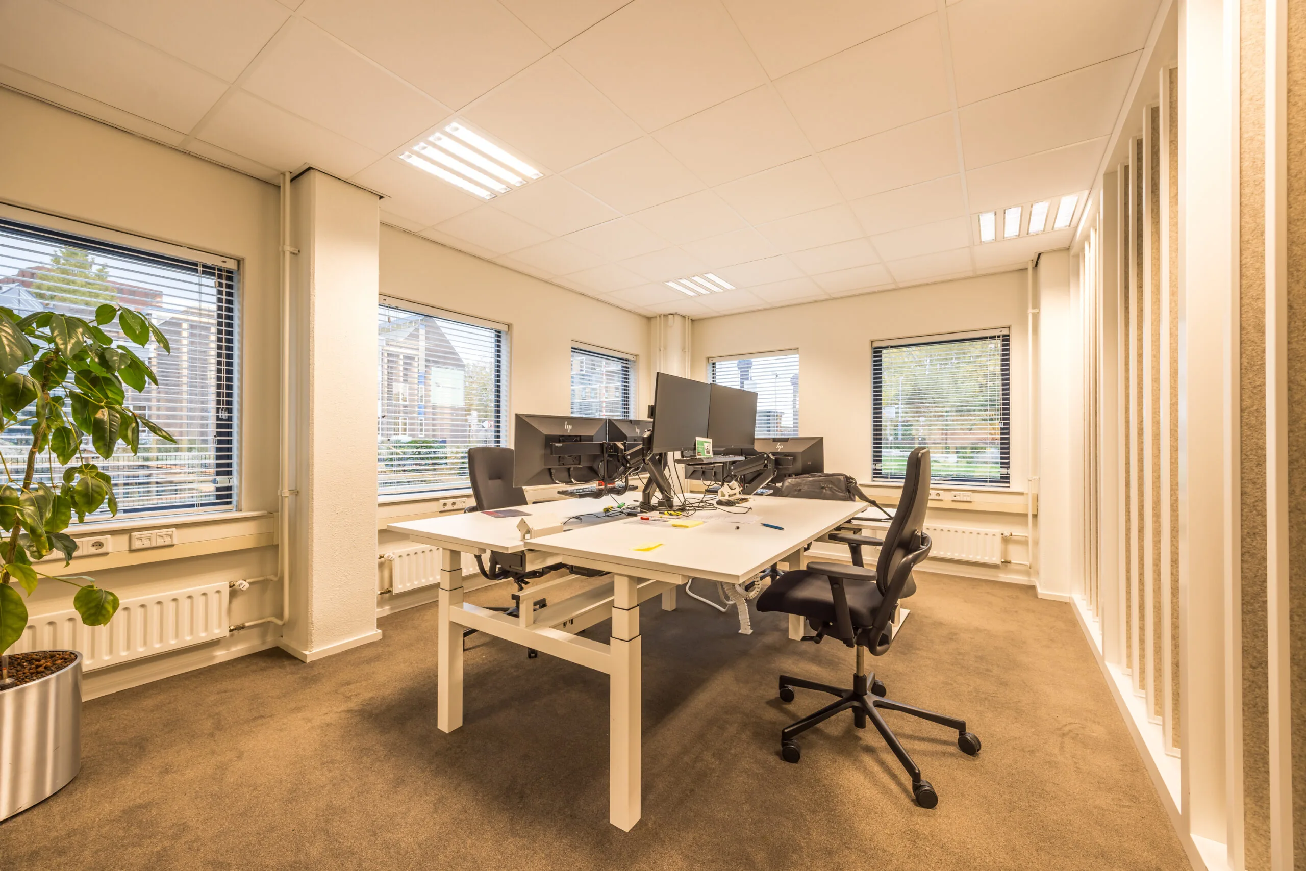 Modern office space at Krijtwal with shared desks, multiple monitors, ergonomic chairs, and large windows providing natural light.