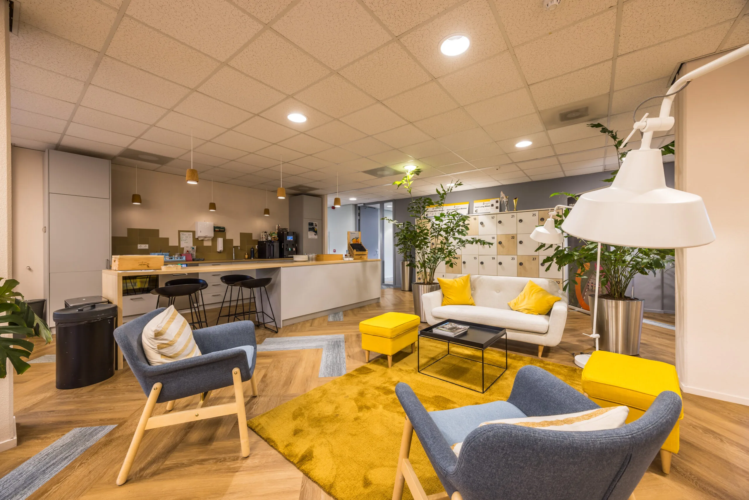 Modern lounge area at Krijtwal featuring cozy seating, vibrant yellow accents, and a kitchenette in the background.