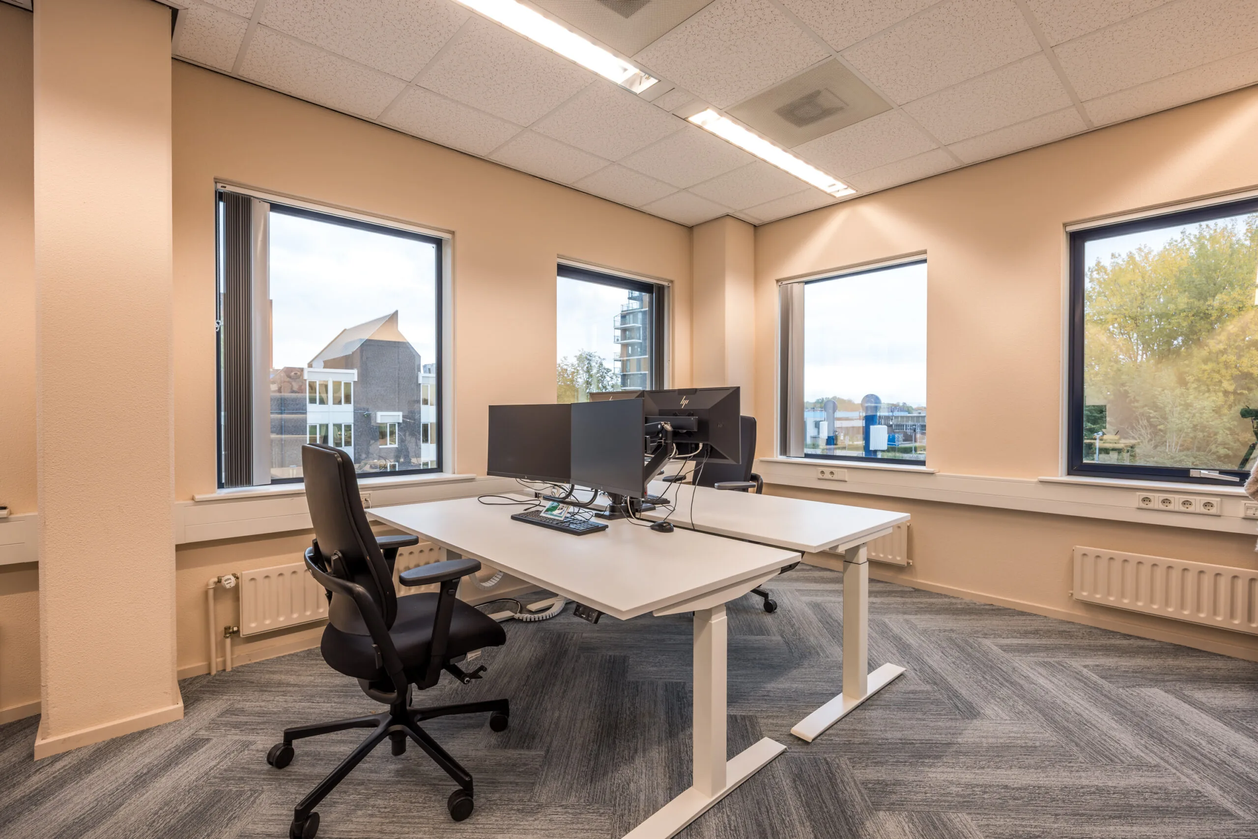 Modern office workspace with dual monitors, ergonomic chairs, and large windows in an office at Krijtwal.