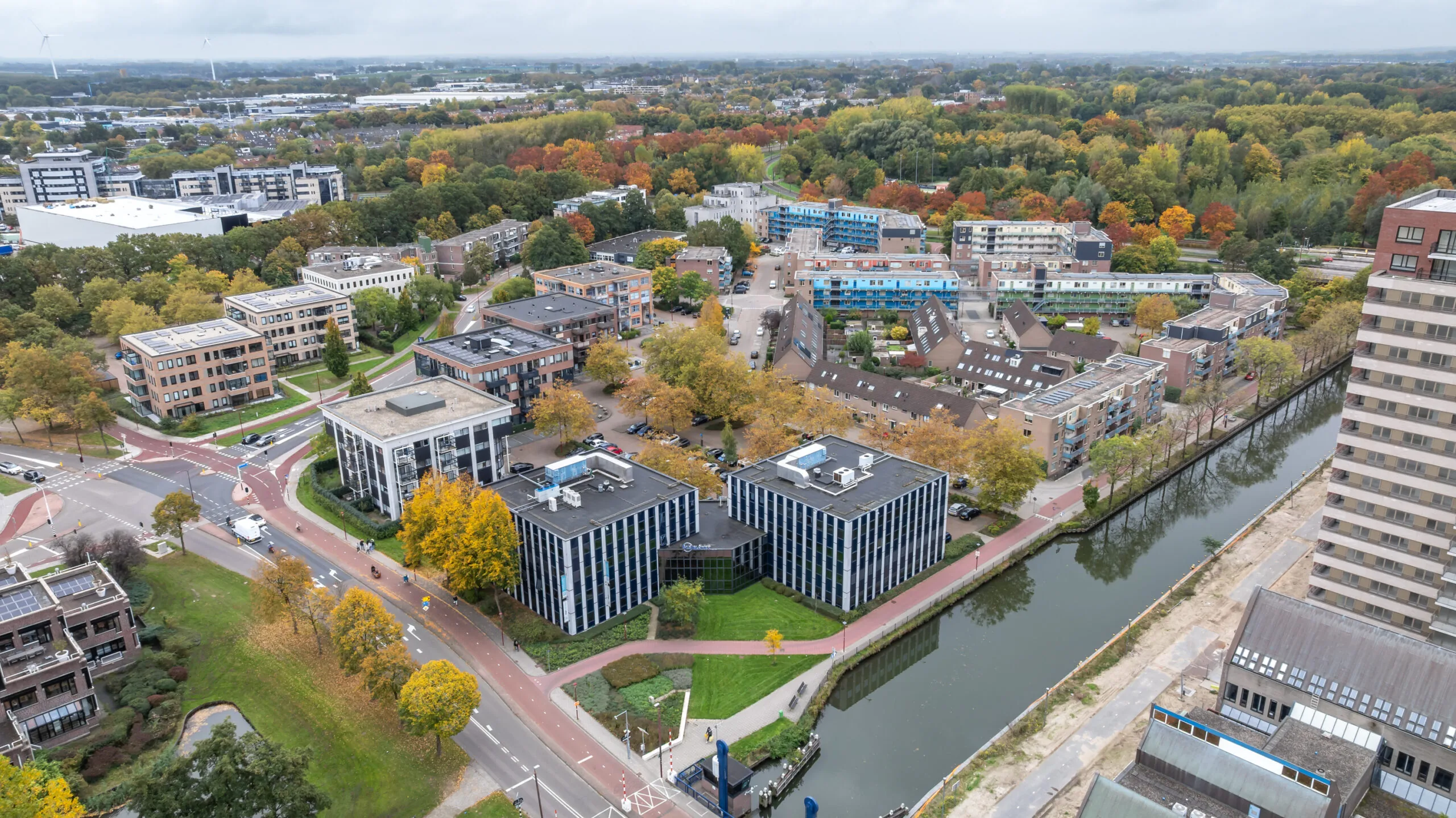 Aerial view of the Krijtwal area featuring modern office buildings, residential housing, and a canal lined with autumn-colored trees.