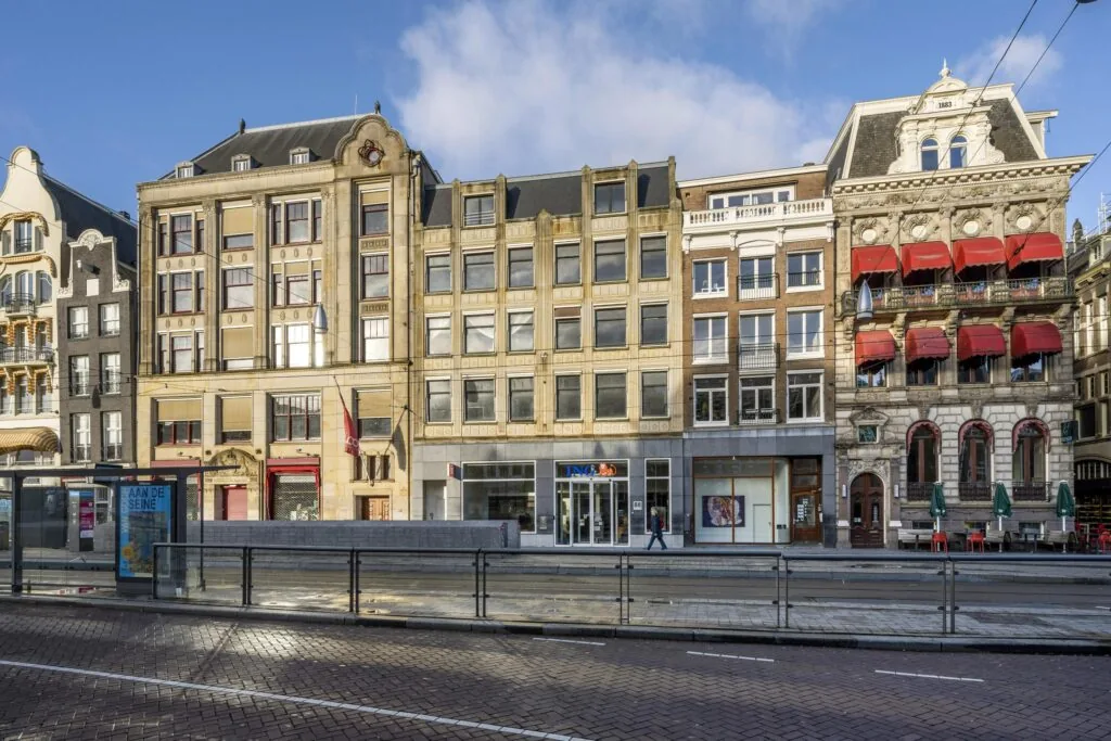 Street view of historic buildings along Rokin in Amsterdam, featuring a tram stop and shops at ground level.