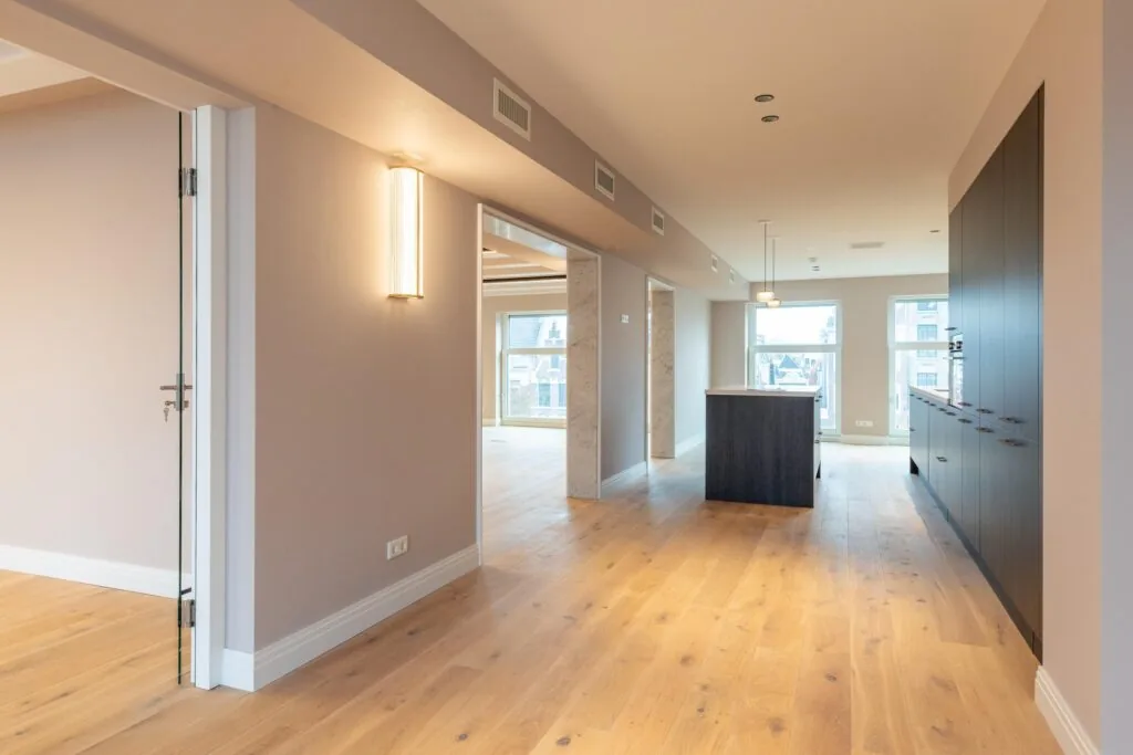 Modern open-plan apartment interior on Rokin with wooden flooring, built-in kitchen, and large windows.