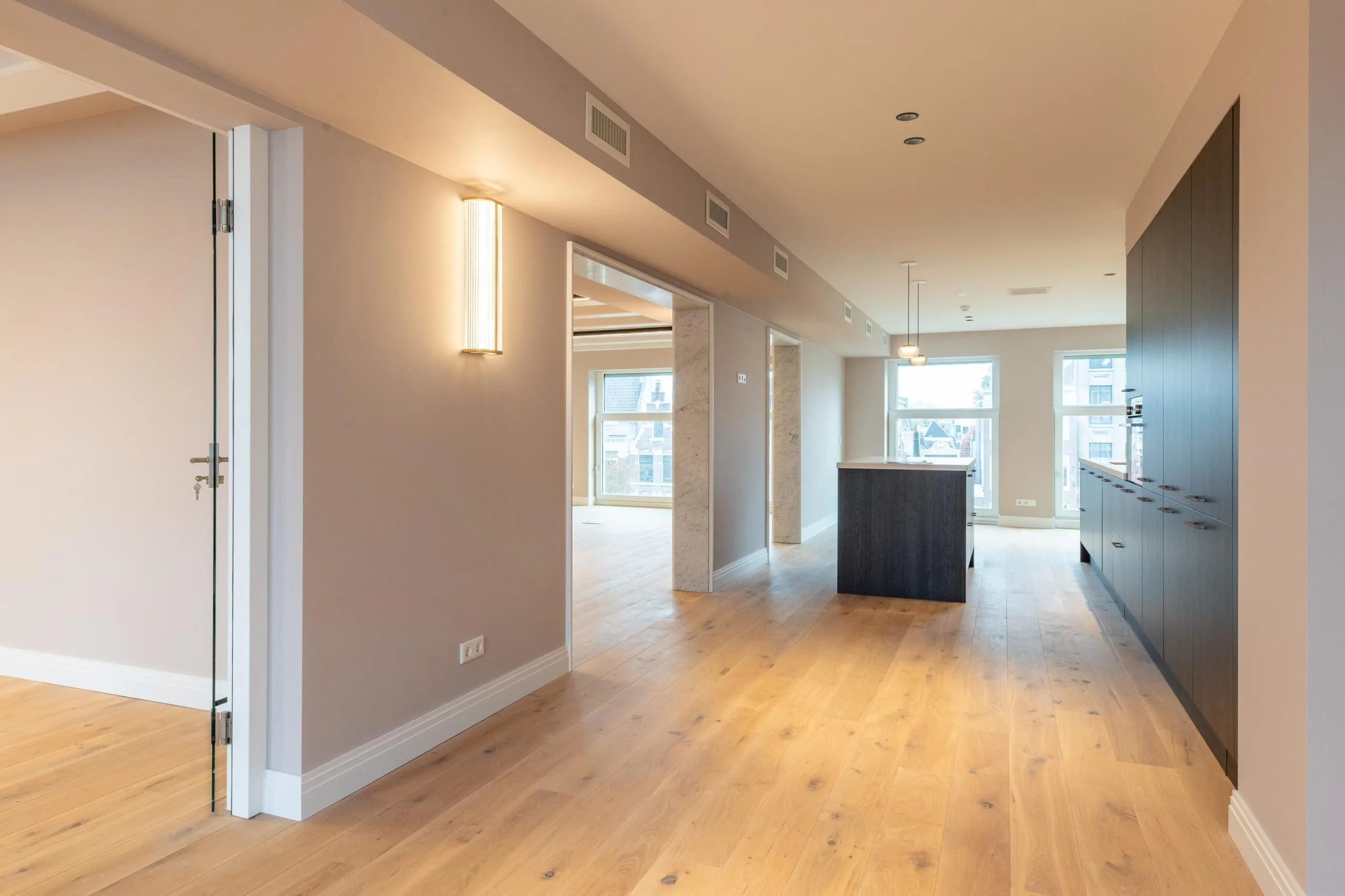 Modern open-plan apartment interior on Rokin with wooden flooring, built-in kitchen, and large windows.