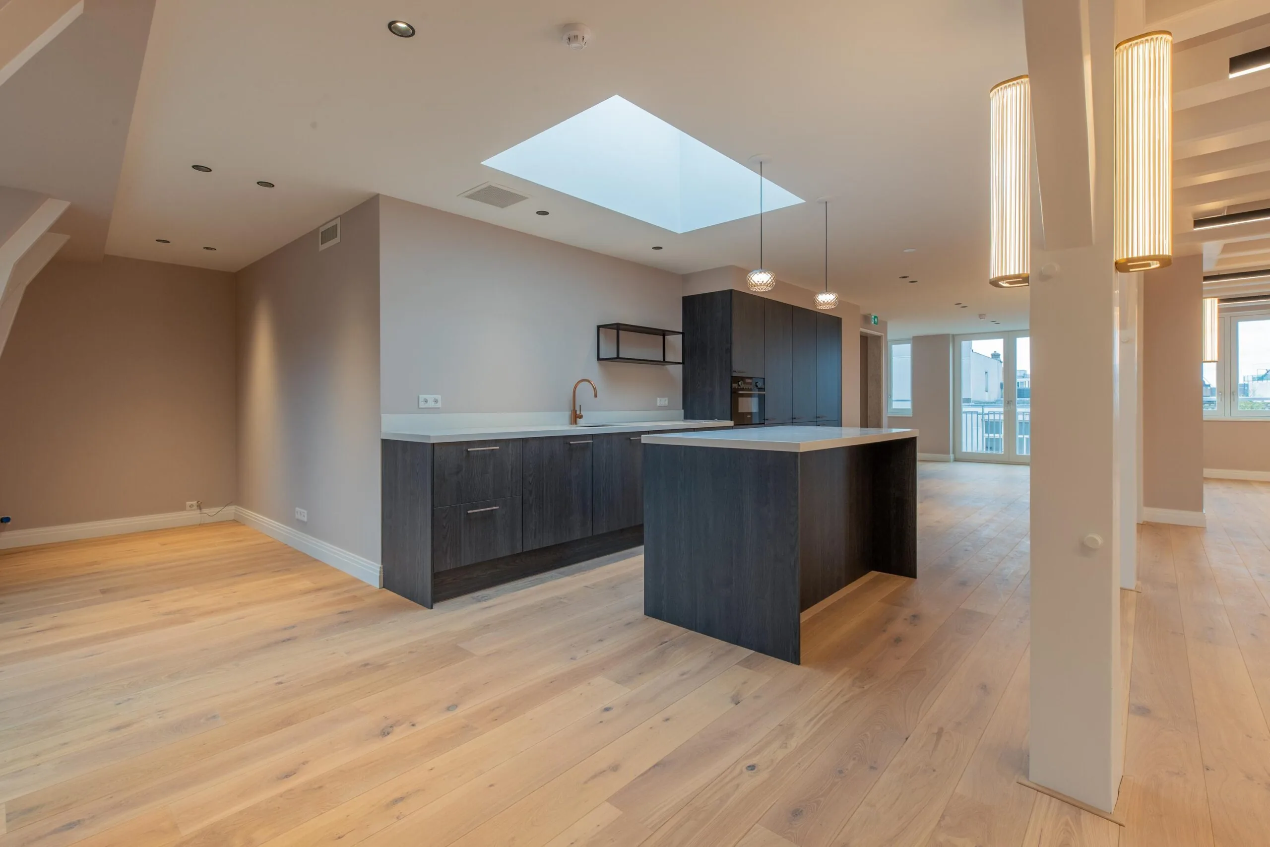 Modern open-plan kitchen and living area with light wooden flooring and dark cabinetry on Rokin.