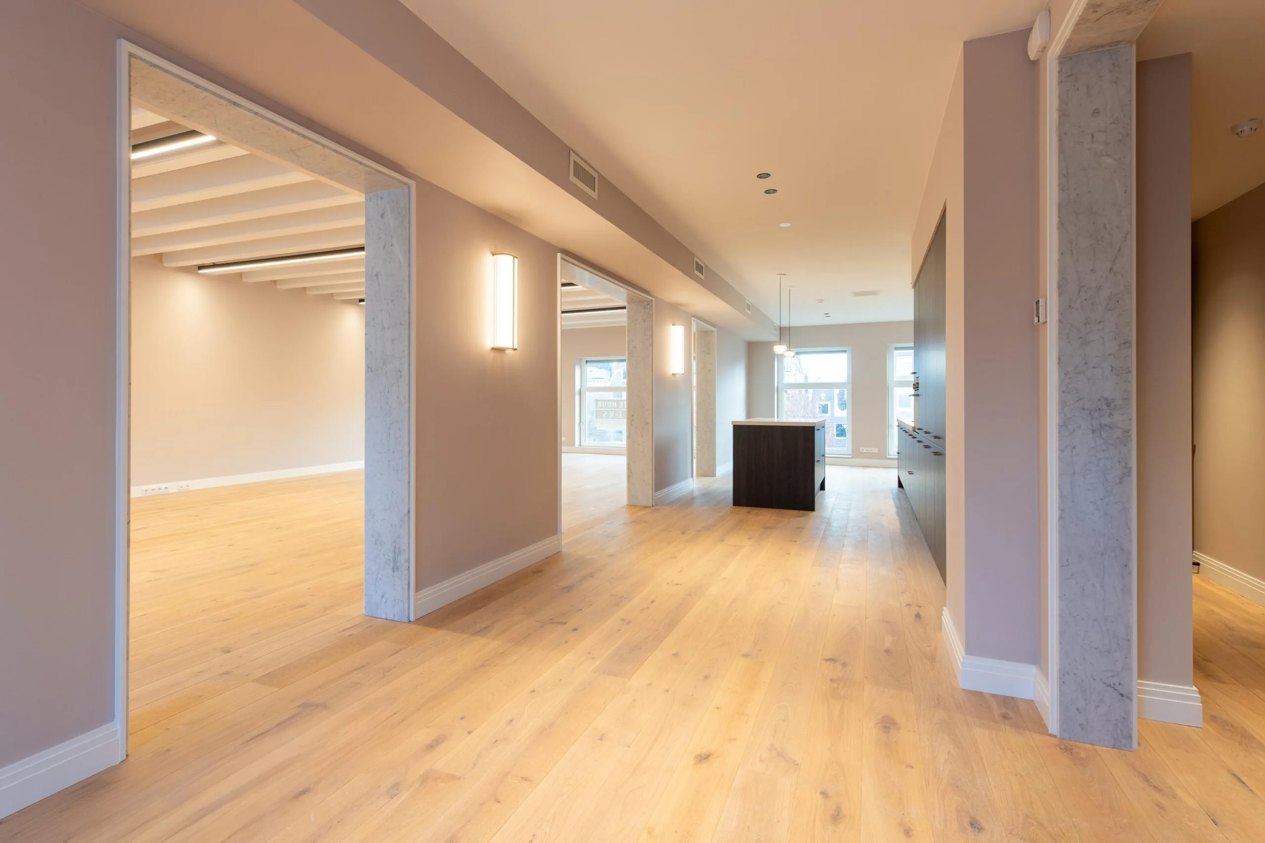 Modern open-plan interior at Rokin featuring light wooden flooring, soft-toned walls, and large windows.