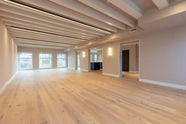 Spacious, modern interior with light wooden flooring, exposed ceiling beams, and large windows on Rokin in Amsterdam.