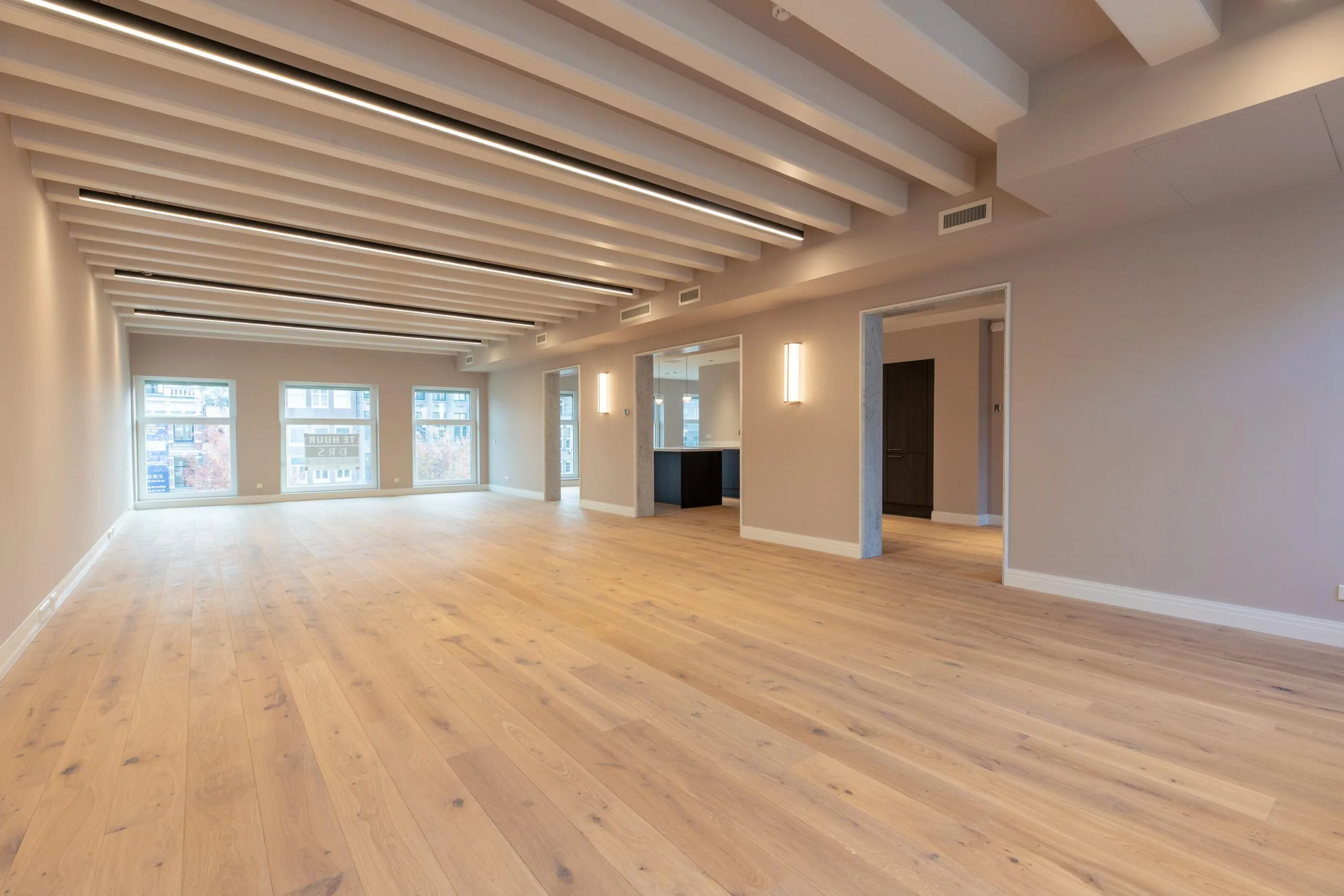 Spacious, modern interior with light wooden flooring, exposed ceiling beams, and large windows on Rokin in Amsterdam.