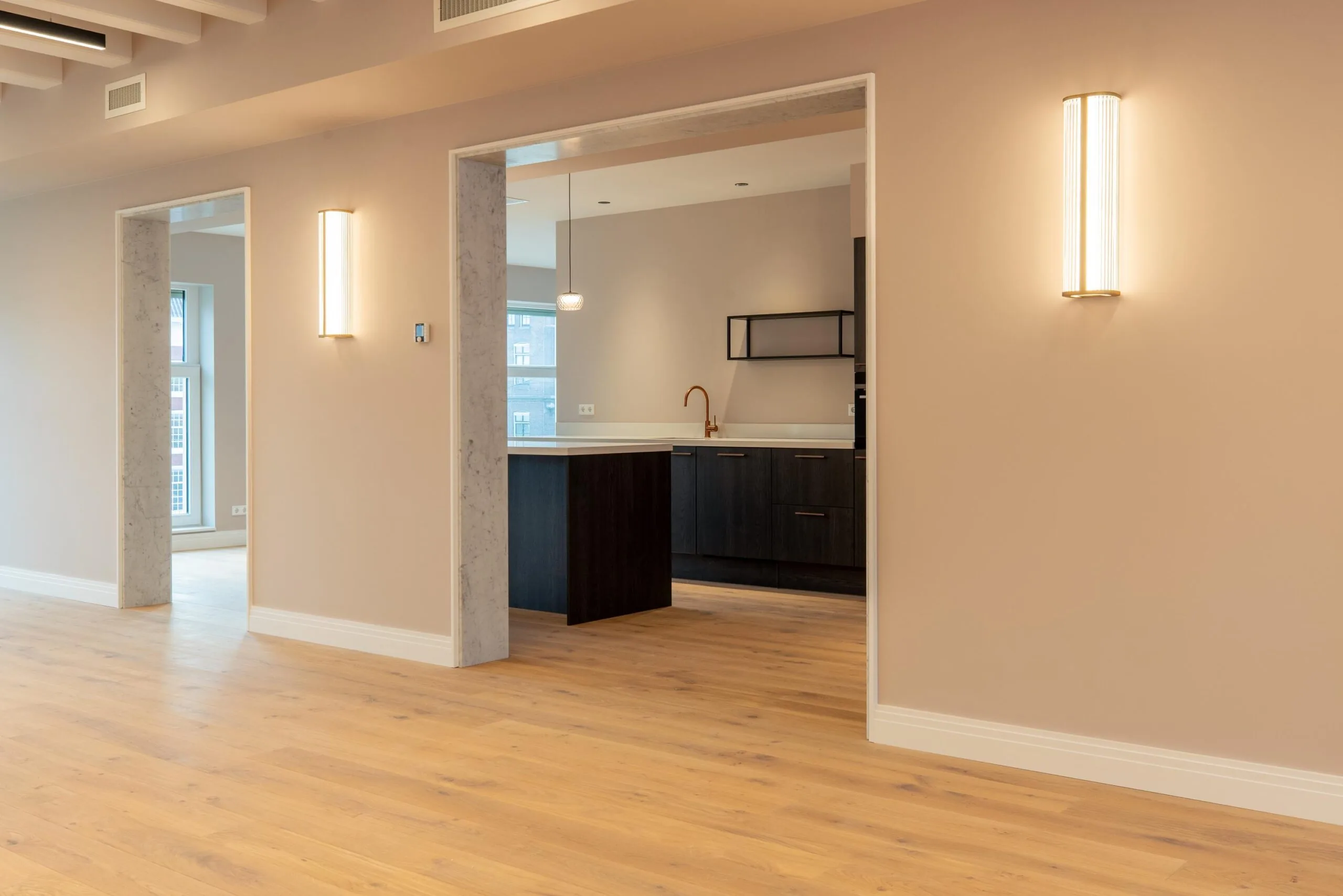 Modern interior of an apartment on Rokin with wooden flooring, beige walls, and a view into a sleek dark kitchen.