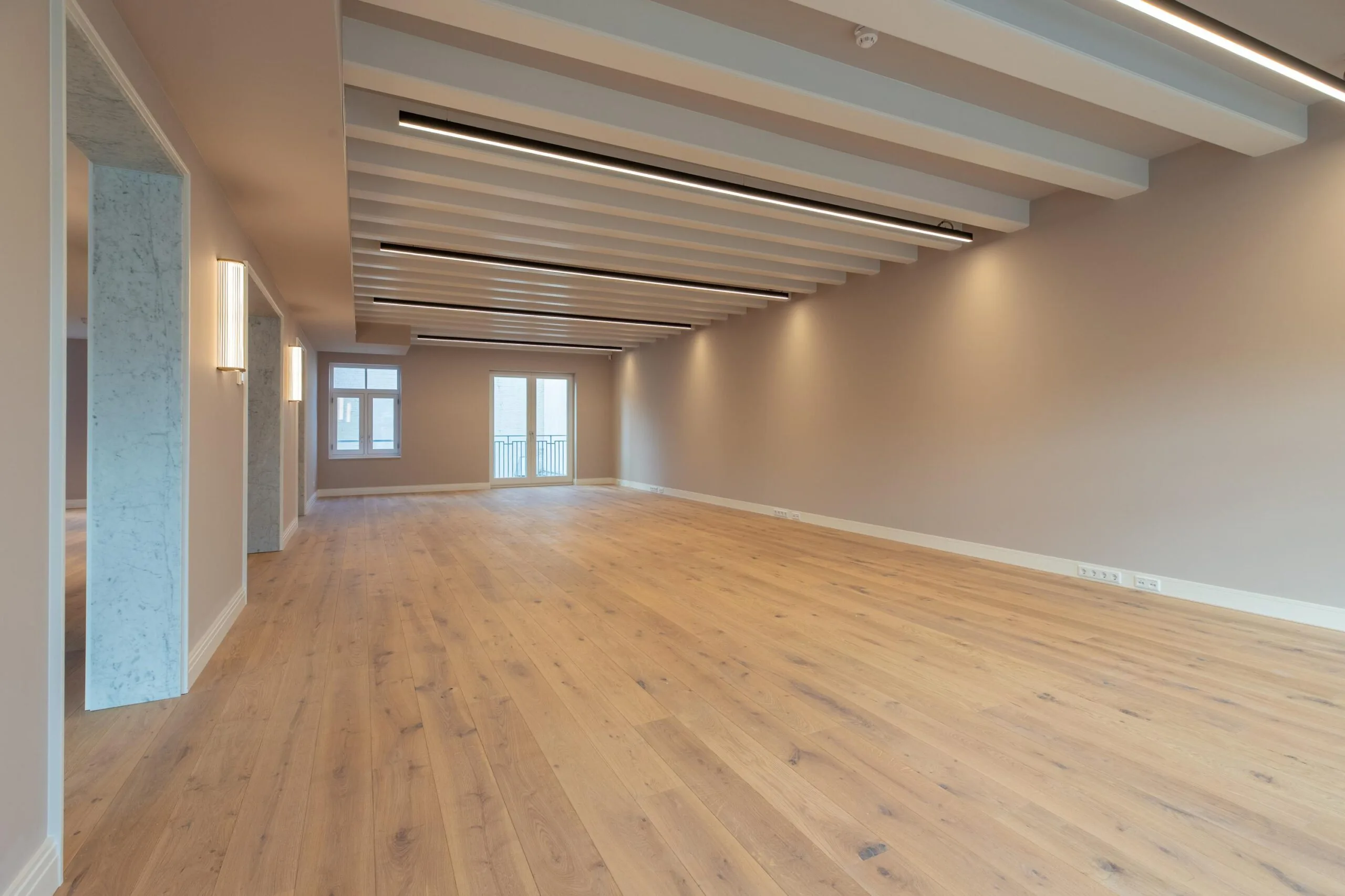 Spacious, modern interior with light wooden flooring, exposed ceiling beams, and large windows at Rokin 176 in Amsterdam.