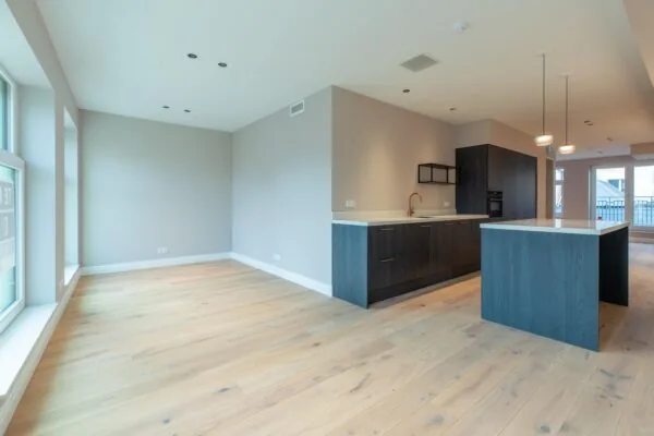 Modern open-plan apartment with light wooden flooring, large windows, and a dark-toned kitchen on Rokin.