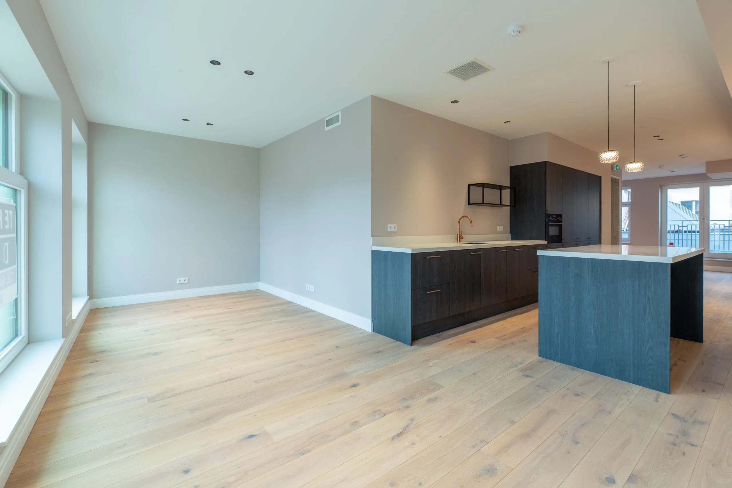 Modern open-plan apartment with light wooden flooring, large windows, and a dark-toned kitchen on Rokin.