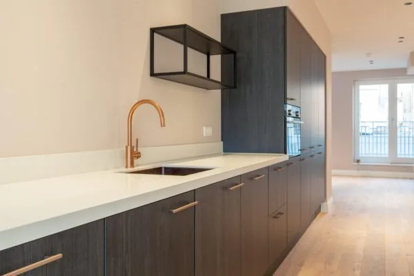 Modern kitchen interior at Rokin with dark wood cabinets, white countertop, and a copper faucet.