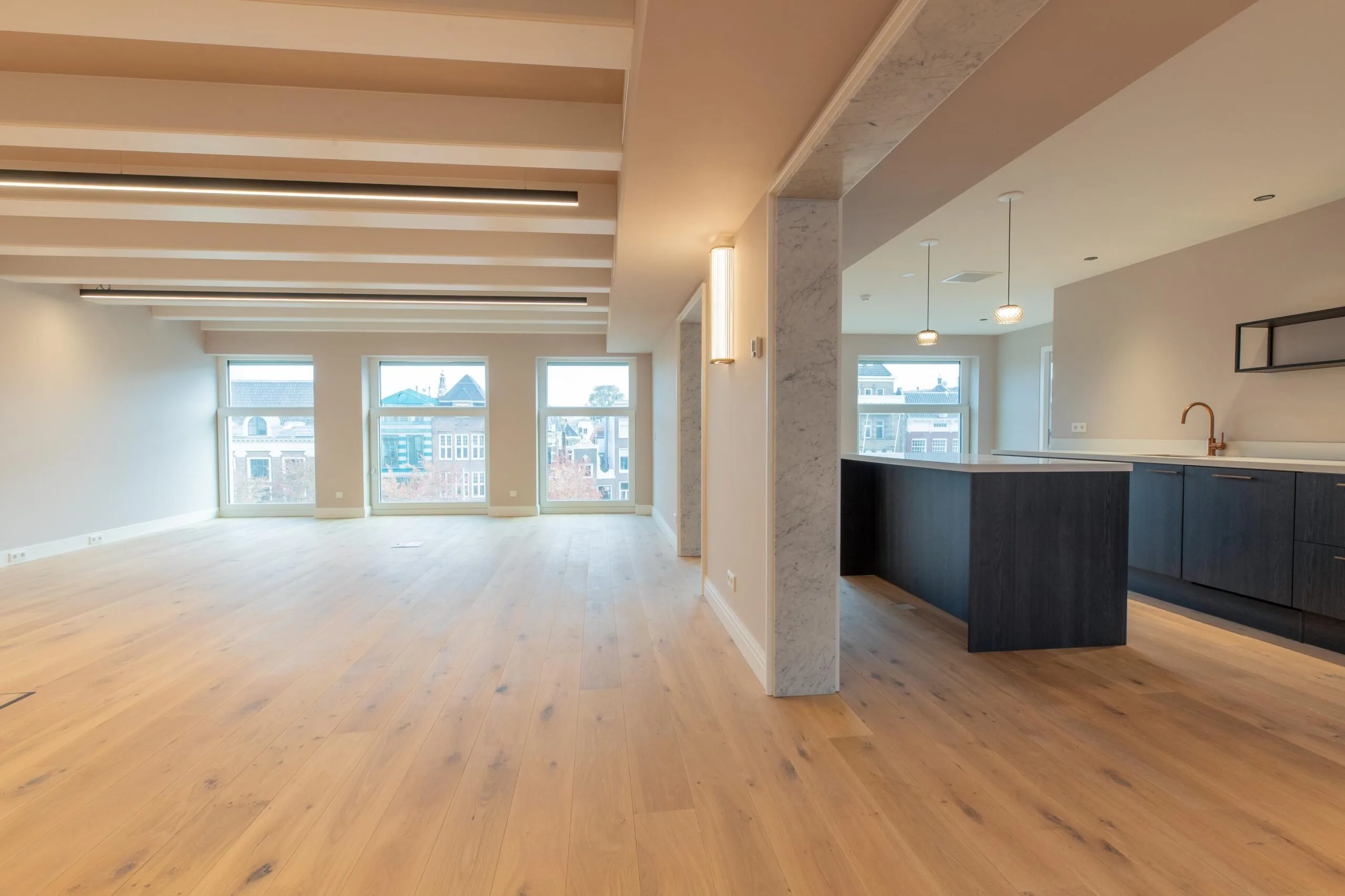 Modern open-plan apartment on Rokin with large windows, wooden flooring, and a sleek dark kitchen island.