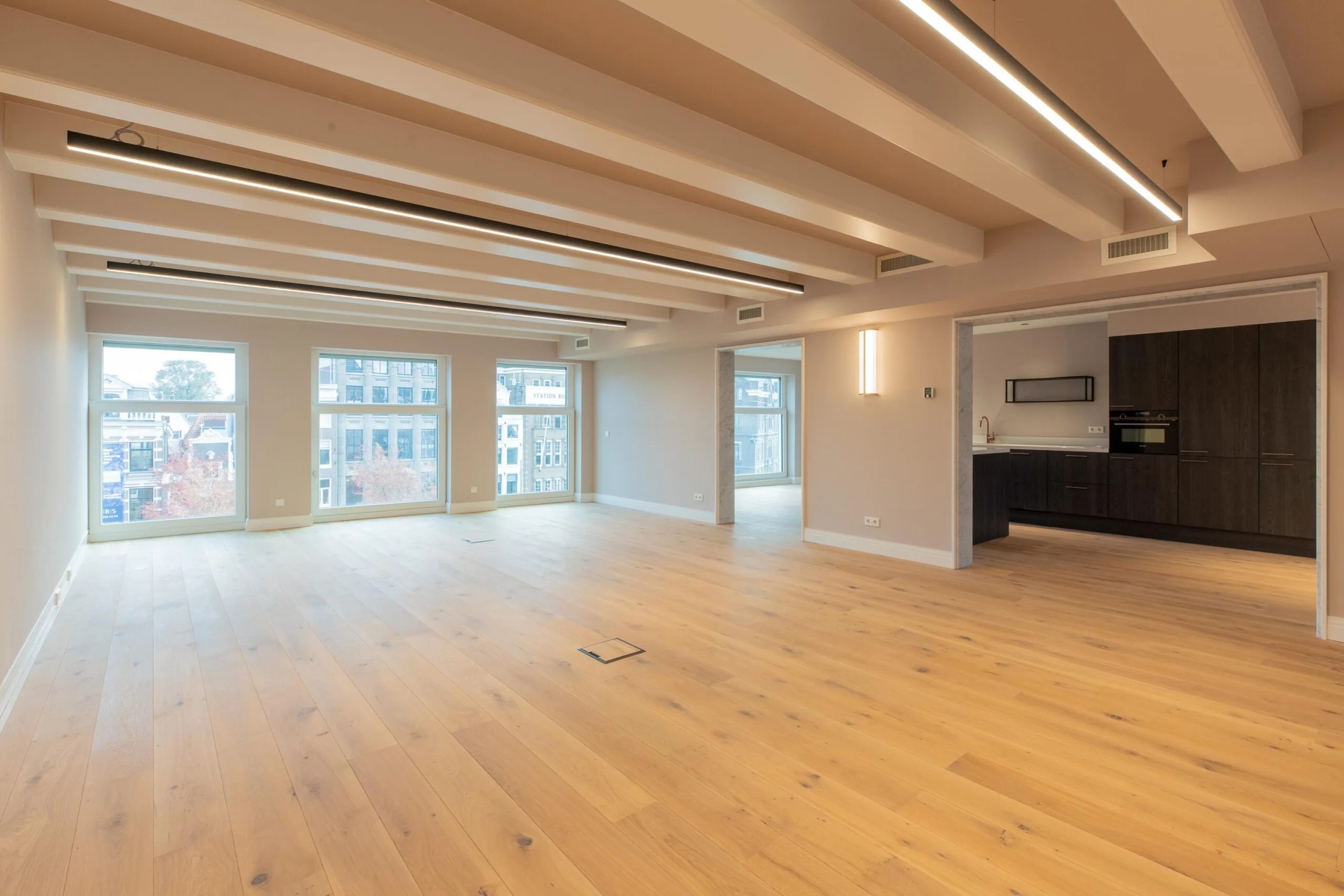 Modern open-plan apartment on Rokin with large windows, wooden flooring, and a sleek built-in kitchen.