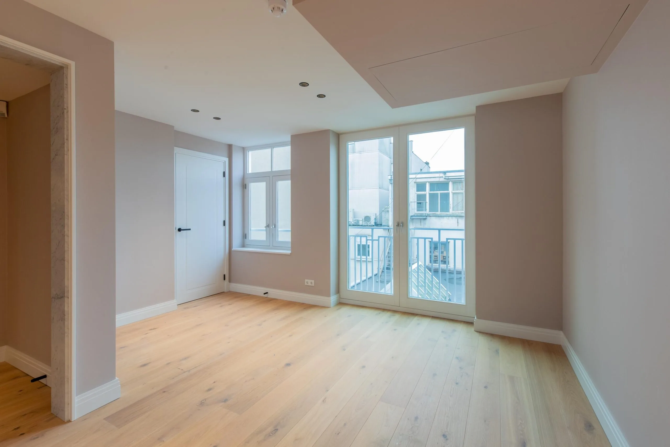 Bright, modern apartment room at Rokin with light wooden flooring, large windows, and access to a small balcony.