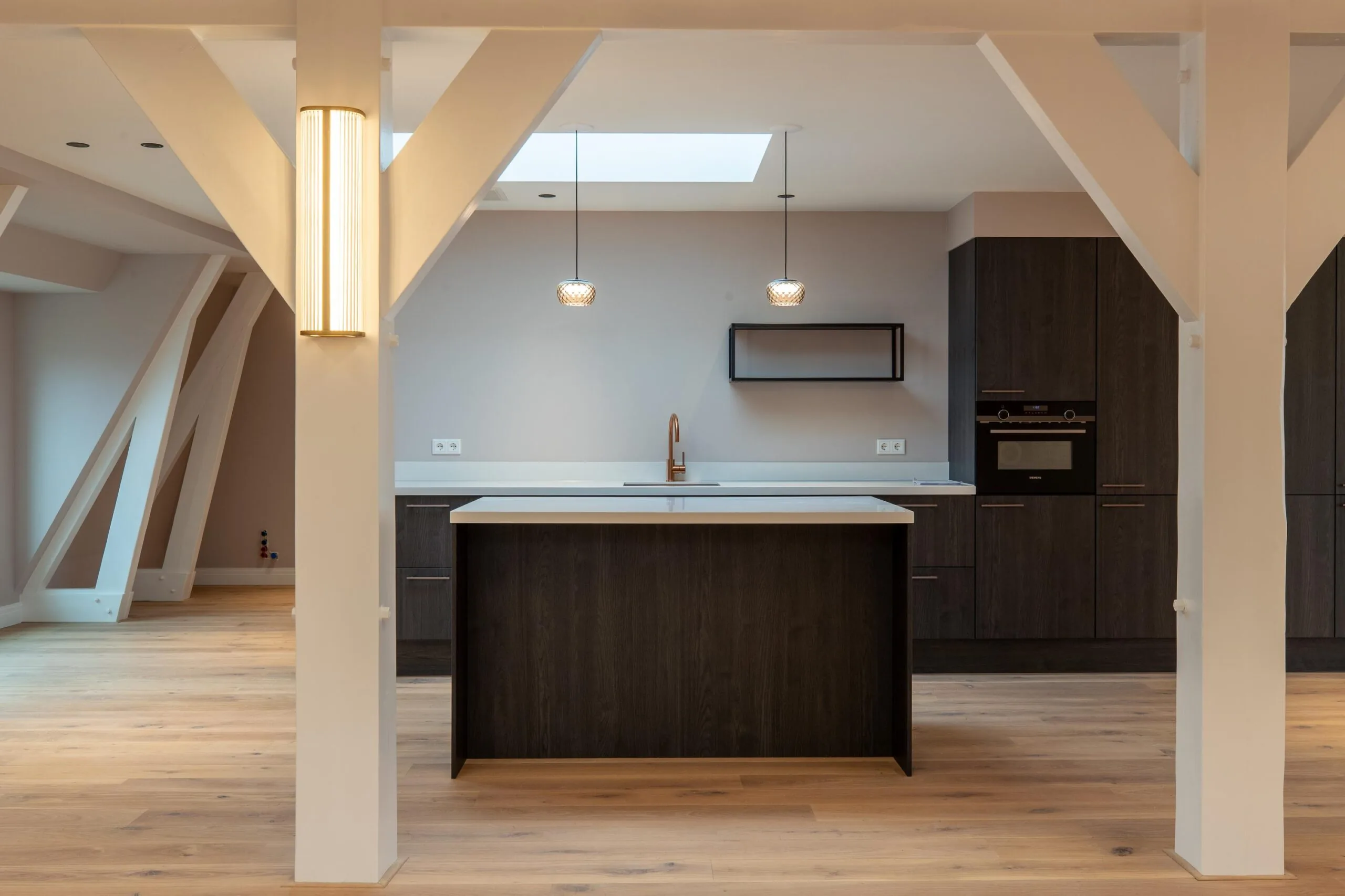 Modern open kitchen with dark wood cabinets, a central island, pendant lights, and exposed white beams.