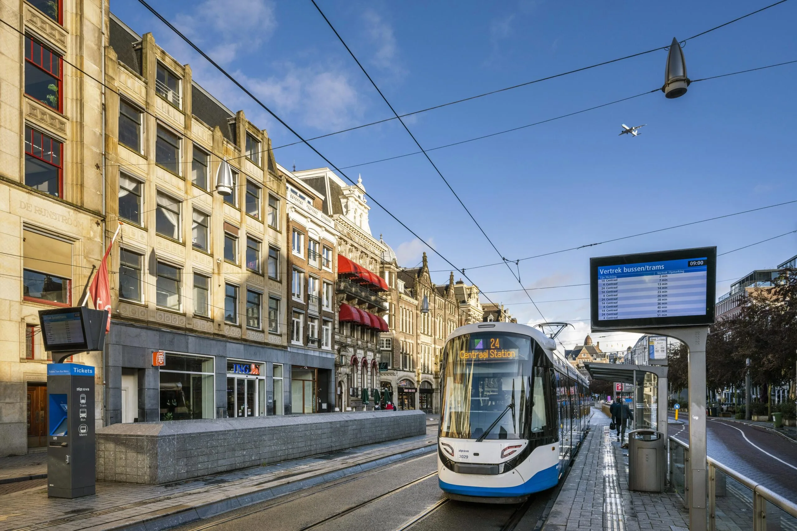 Tram 24 heading to Centraal Station arrives at the Rokin stop in Amsterdam on a clear morning.