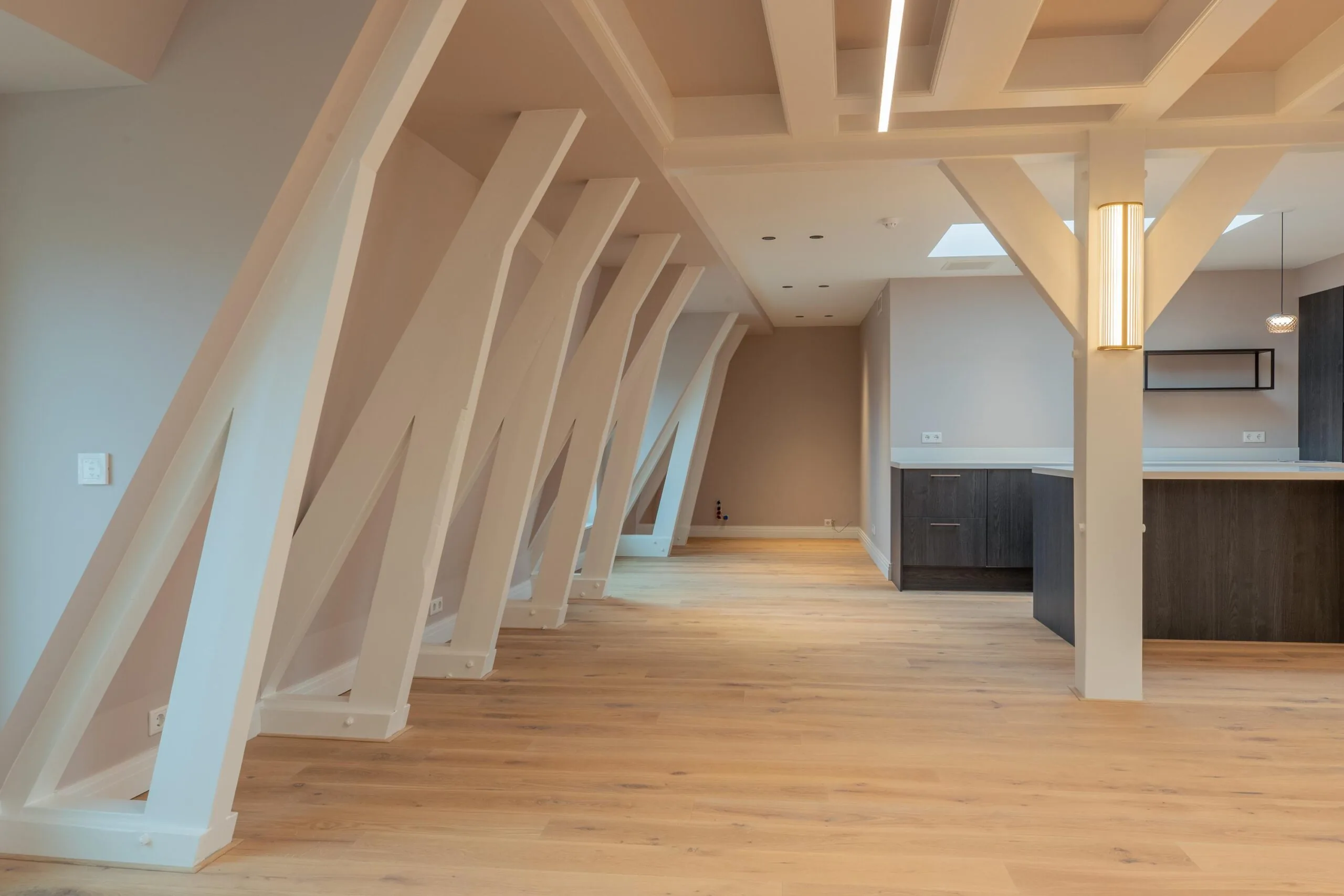 Modern attic apartment on Rokin with slanted white support beams, wooden flooring, and an open kitchen area.