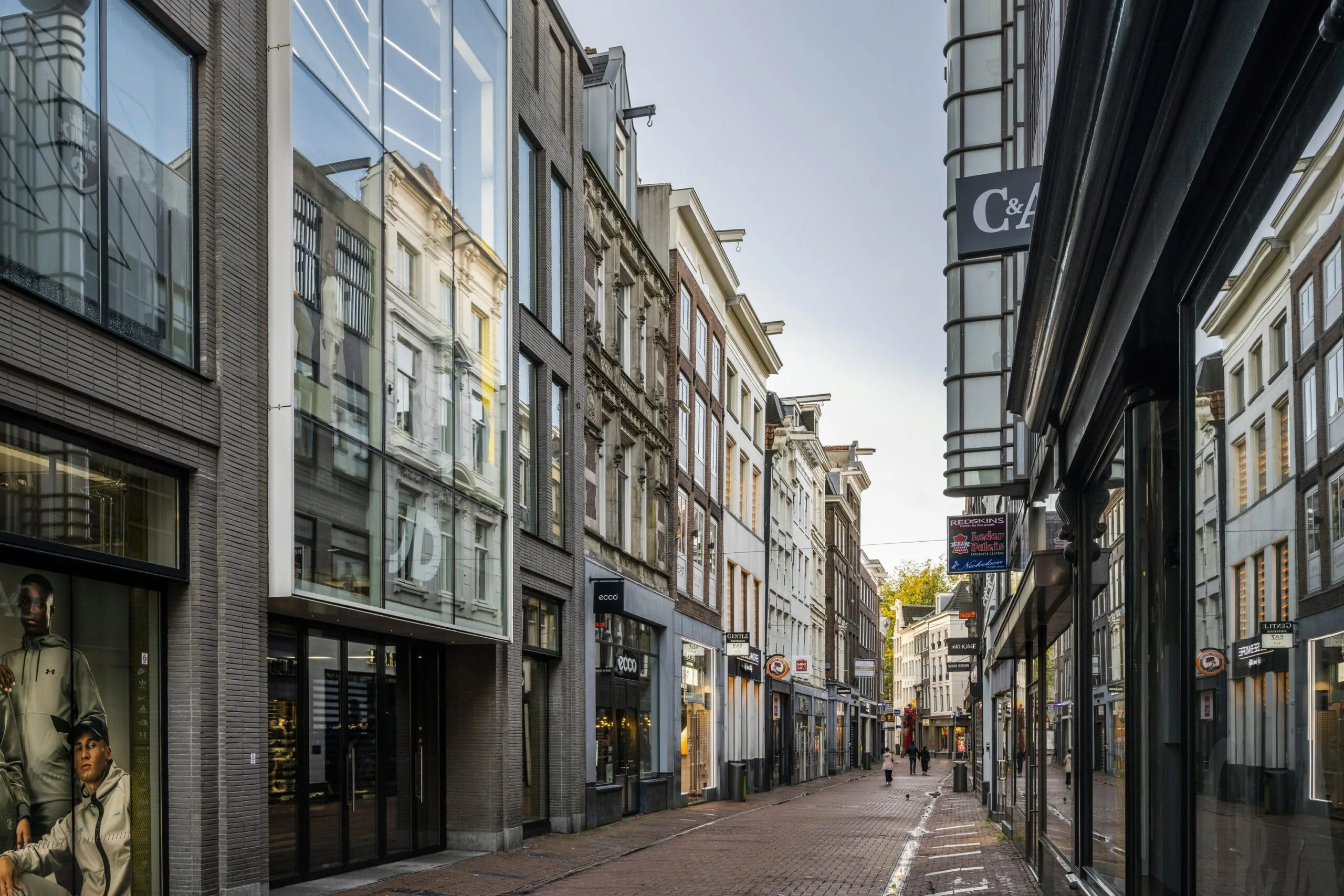 Empty shopping street Rokin in Amsterdam with modern and historic buildings and various retail store signs.