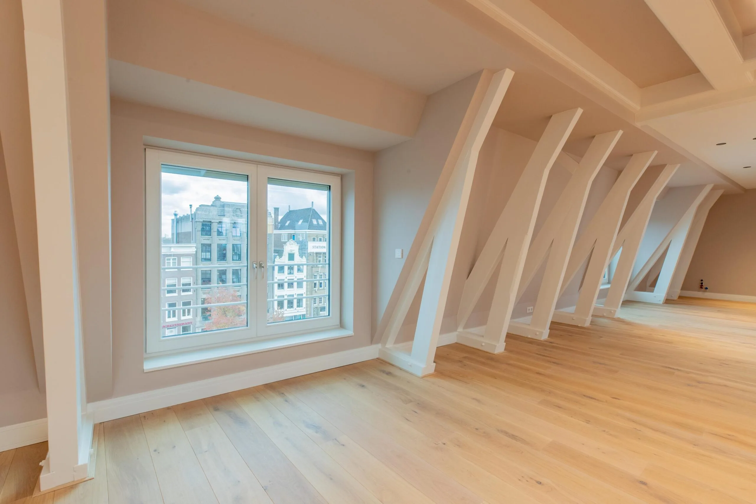 Bright loft-style room with wooden floors, white beams, and a large window overlooking buildings on Rokin in Amsterdam.