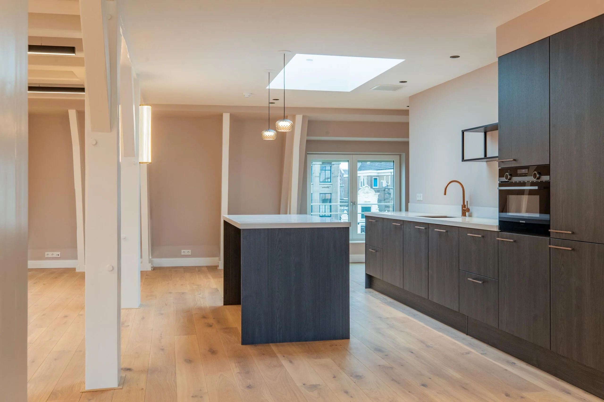 Modern kitchen interior on Rokin with dark wood cabinets, a central island, skylight, and large window offering city views.