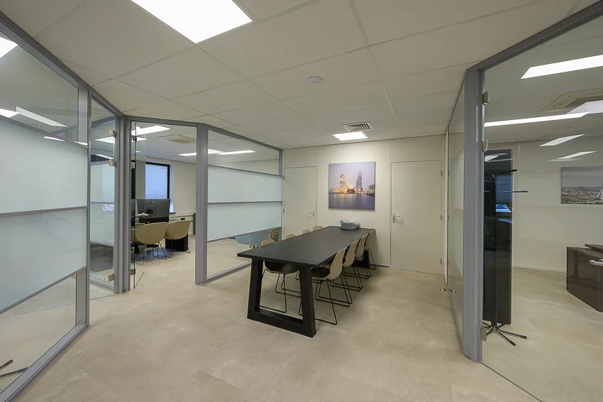 Modern office interior with a black conference table, glass-walled meeting rooms, and neutral-colored decor.