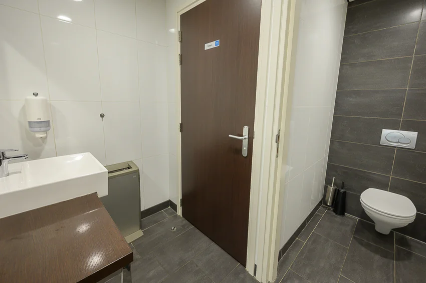 Modern public restroom with a wall-mounted toilet, sink, and a door labeled "toilet" in Dutch.