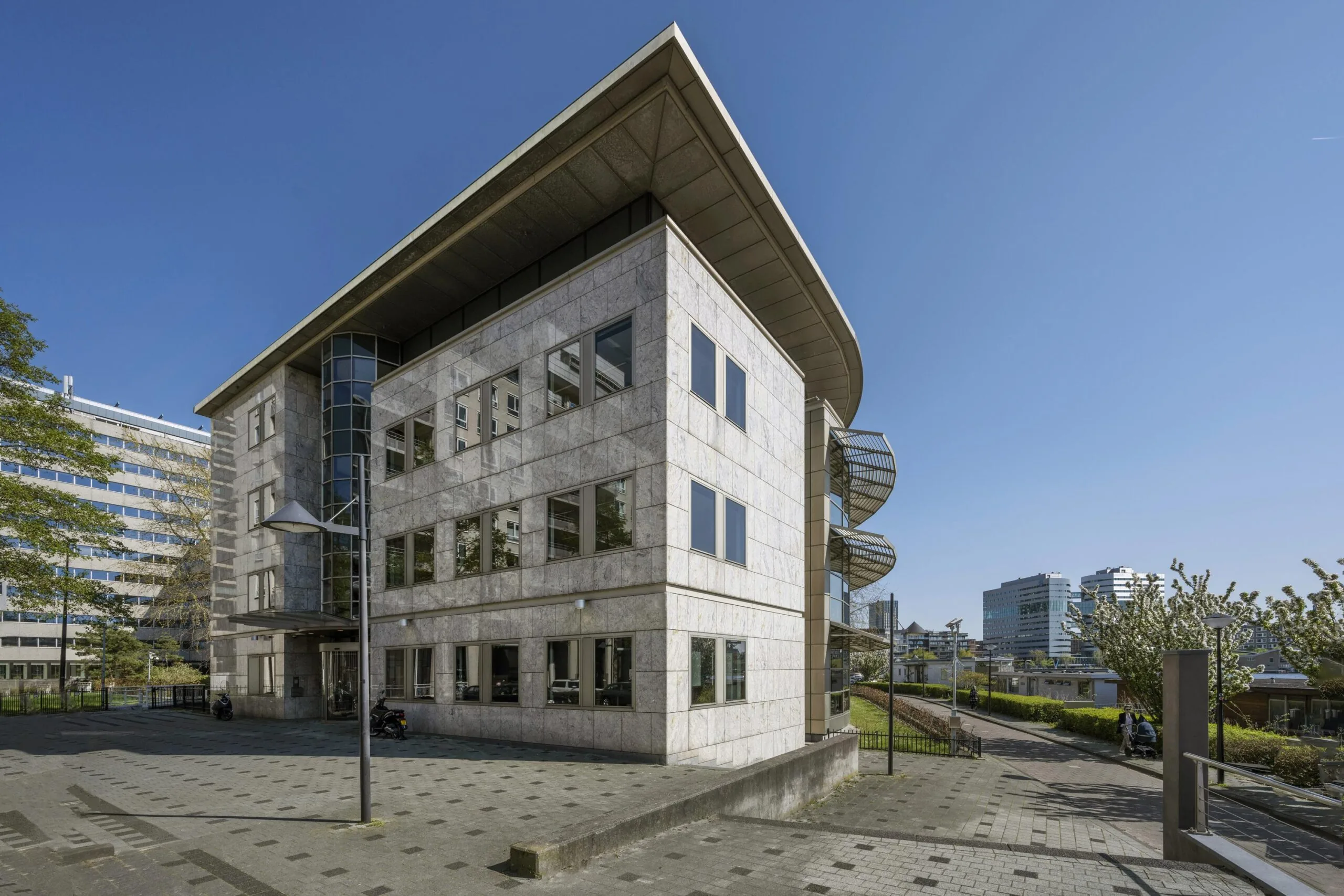 Modern office building at De Omval in Amsterdam under a clear blue sky.