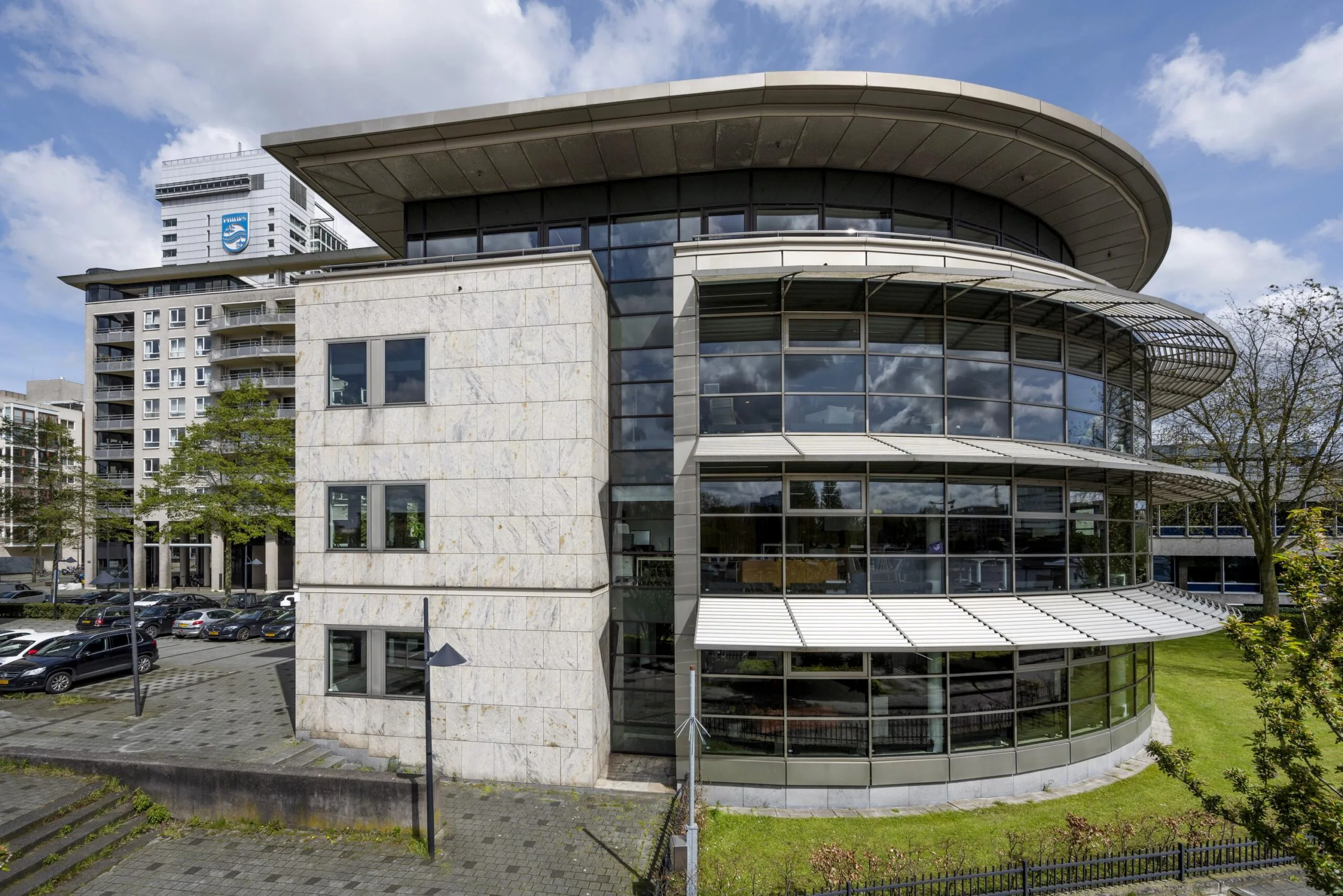 Modern office building "De Omval" with curved glass facade and marble exterior, located in an urban area with adjacent high-rise apartments.