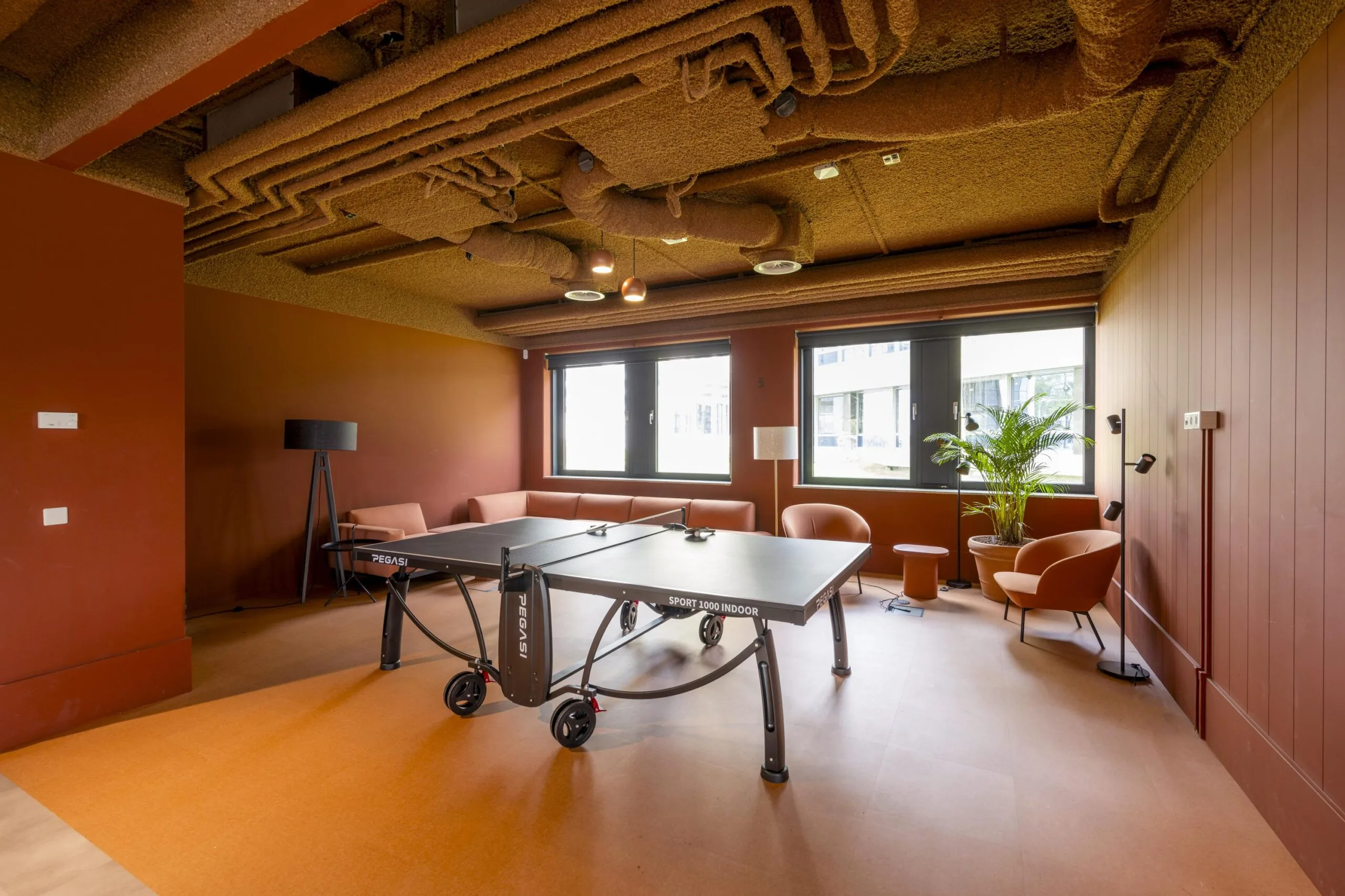 Modern lounge area with a ping pong table, cozy seating, and a warm-toned interior at Omval.