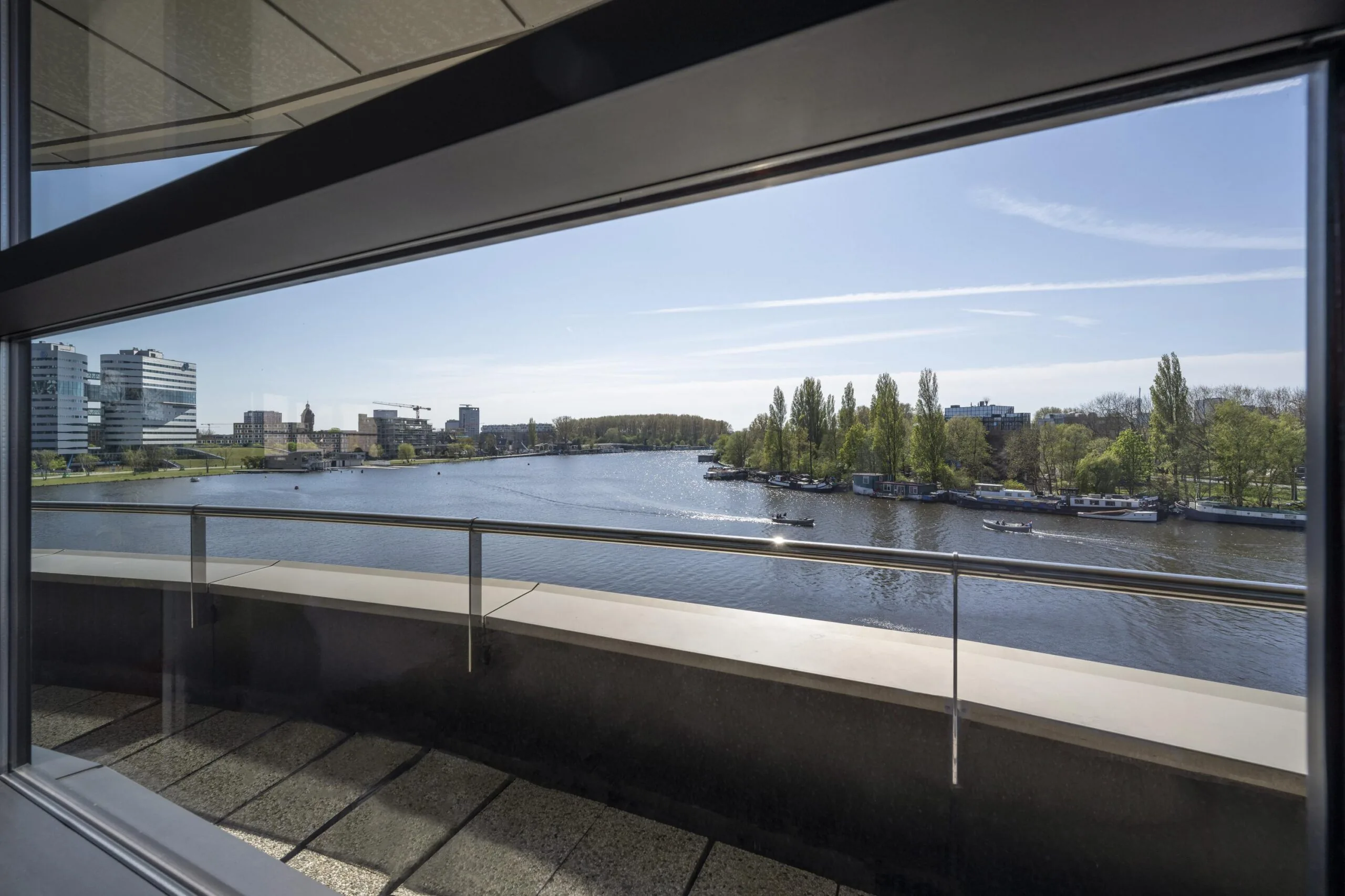 View from the Omval building overlooking the Amstel River with boats and modern office buildings in the distance.