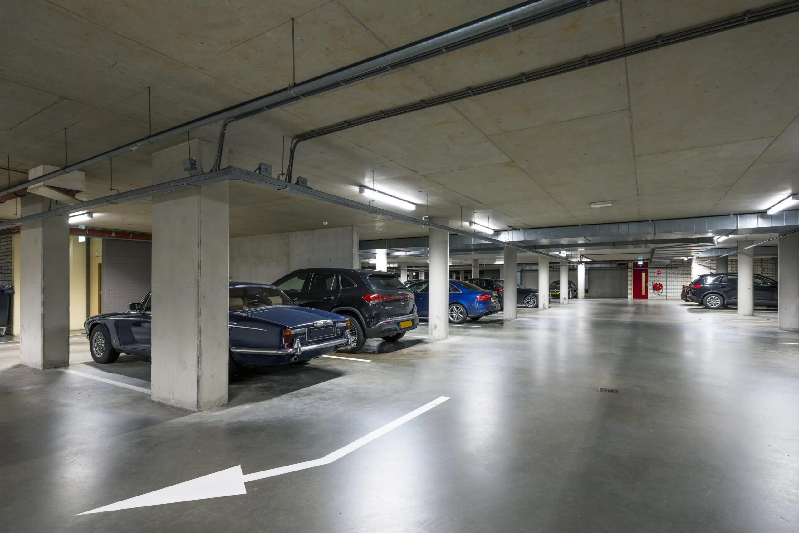 Underground parking garage at Omval 2526 with multiple parked cars and concrete pillars.