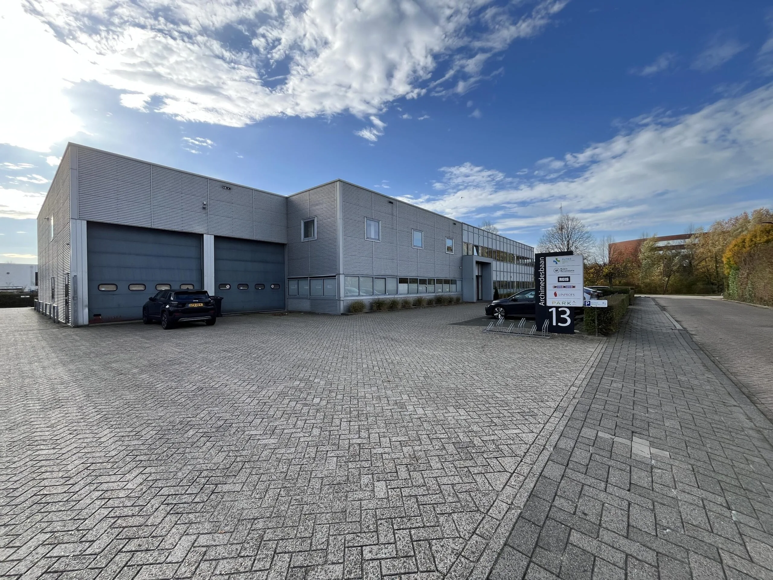 Industrial building at Archimedesbaan 13 with parking area and company sign visible under a partly cloudy sky.