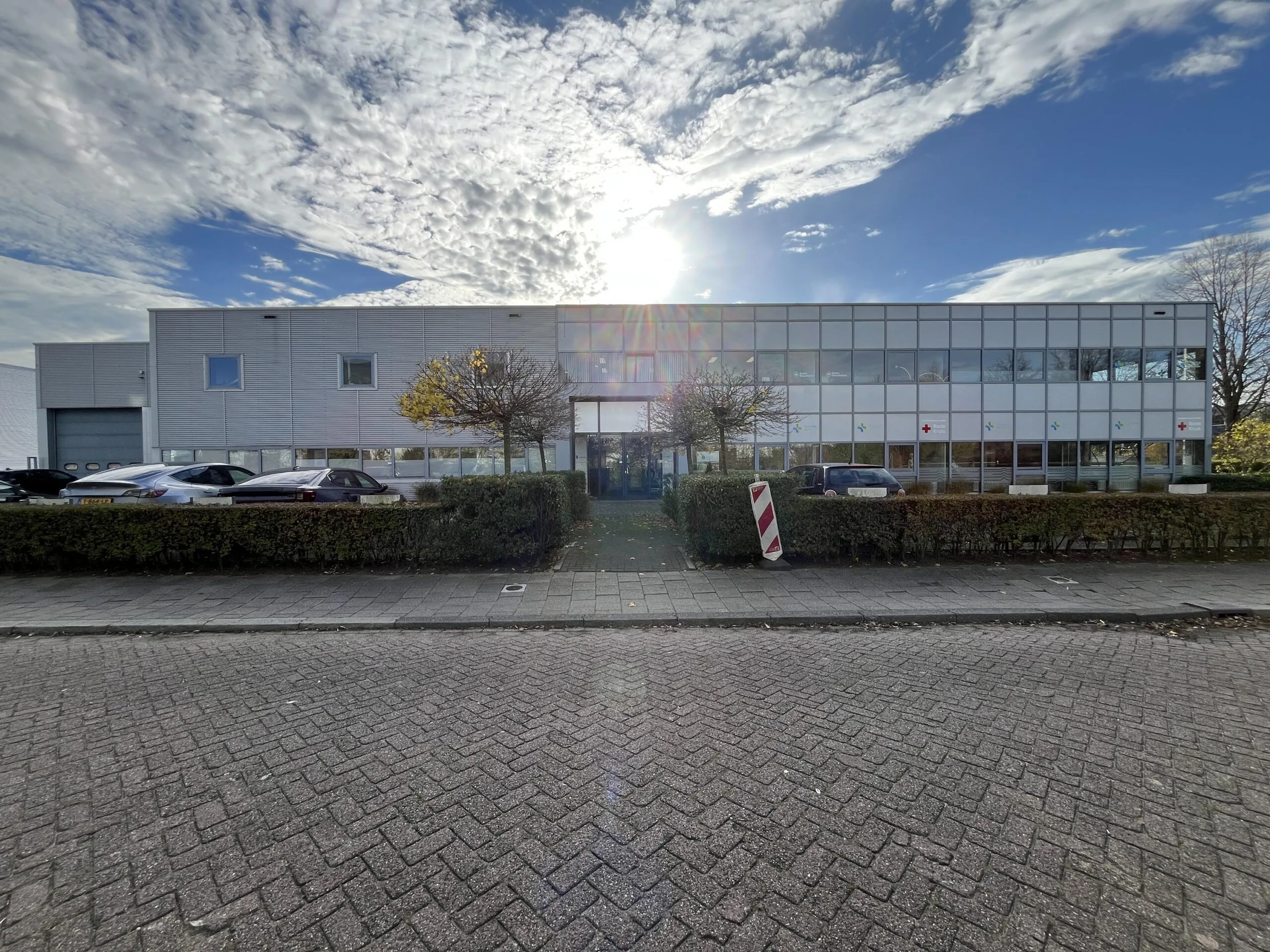 Modern office building on Archimedesbaan with parked cars and a partly cloudy sky.