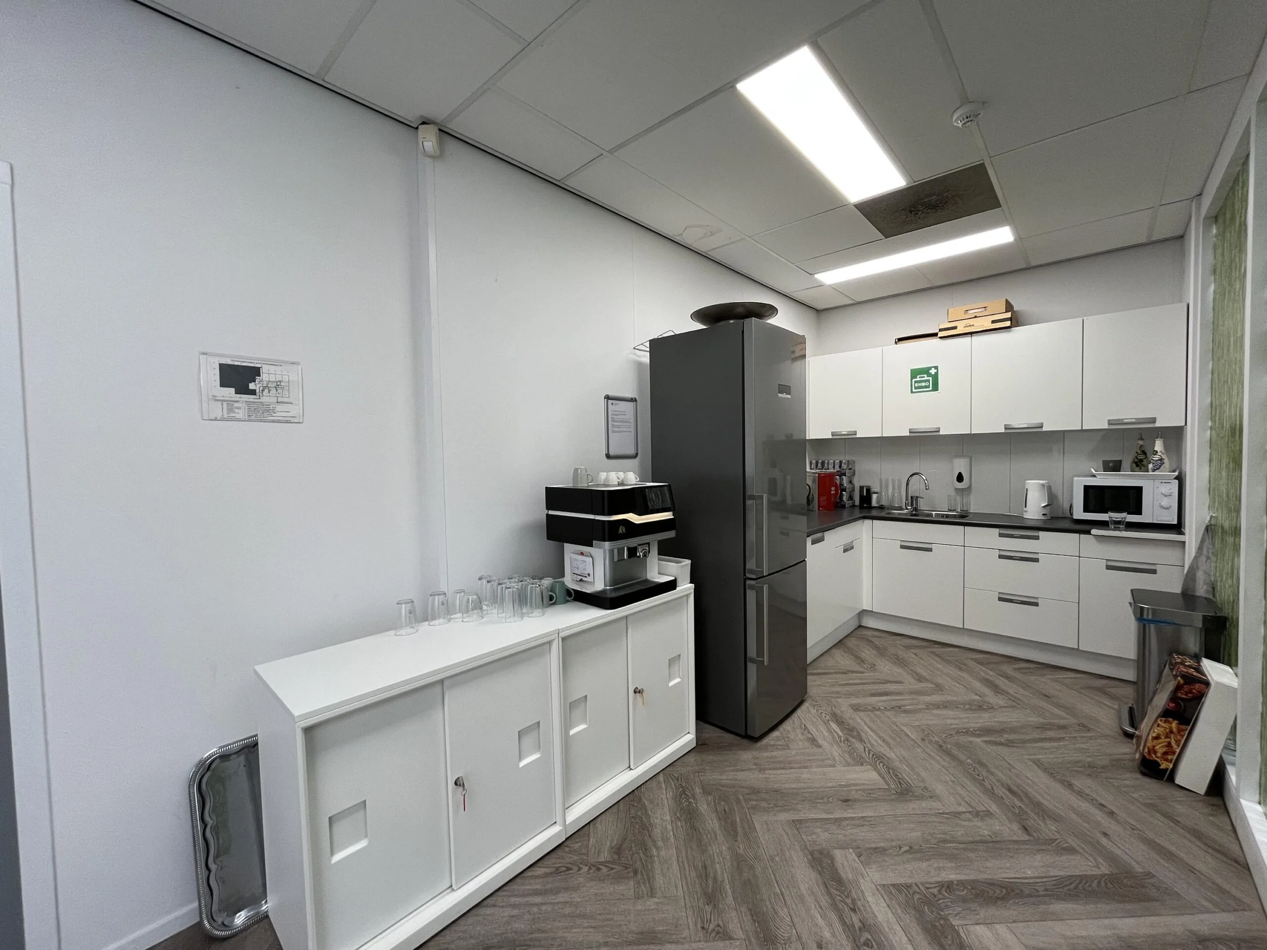 Modern office kitchen at Archimedesbaan with white cabinets, coffee machine, and refrigerator.