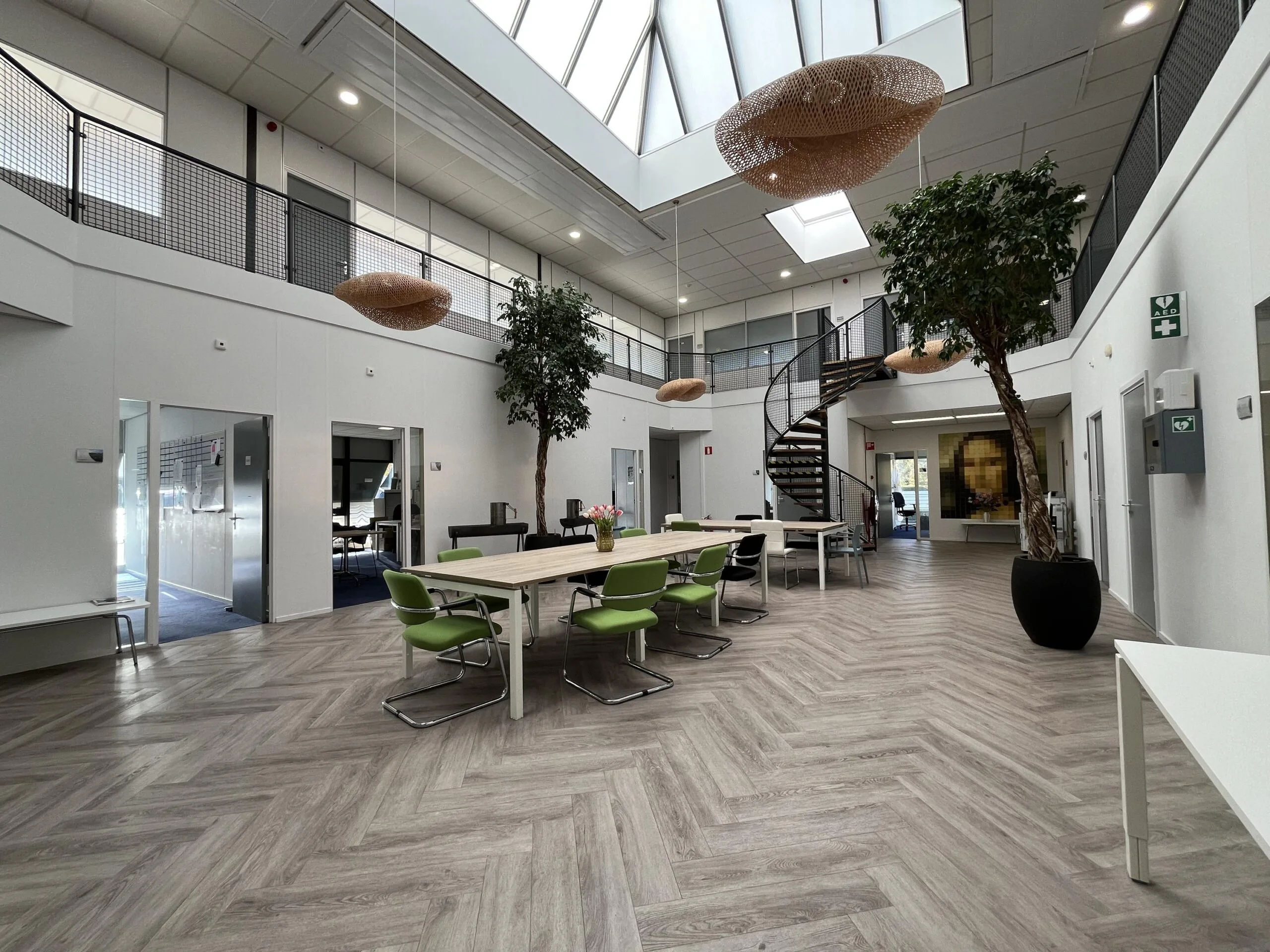 Modern open office space on Archimedesbaan with large skylights, spiral staircase, and communal work tables.