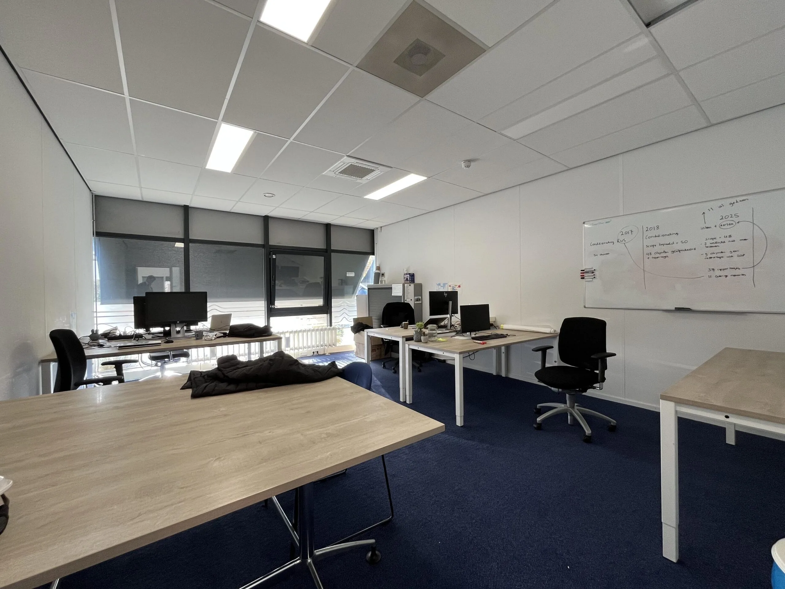 Modern office space on Archimedesbaan with several desks, computer monitors, and a whiteboard with notes.