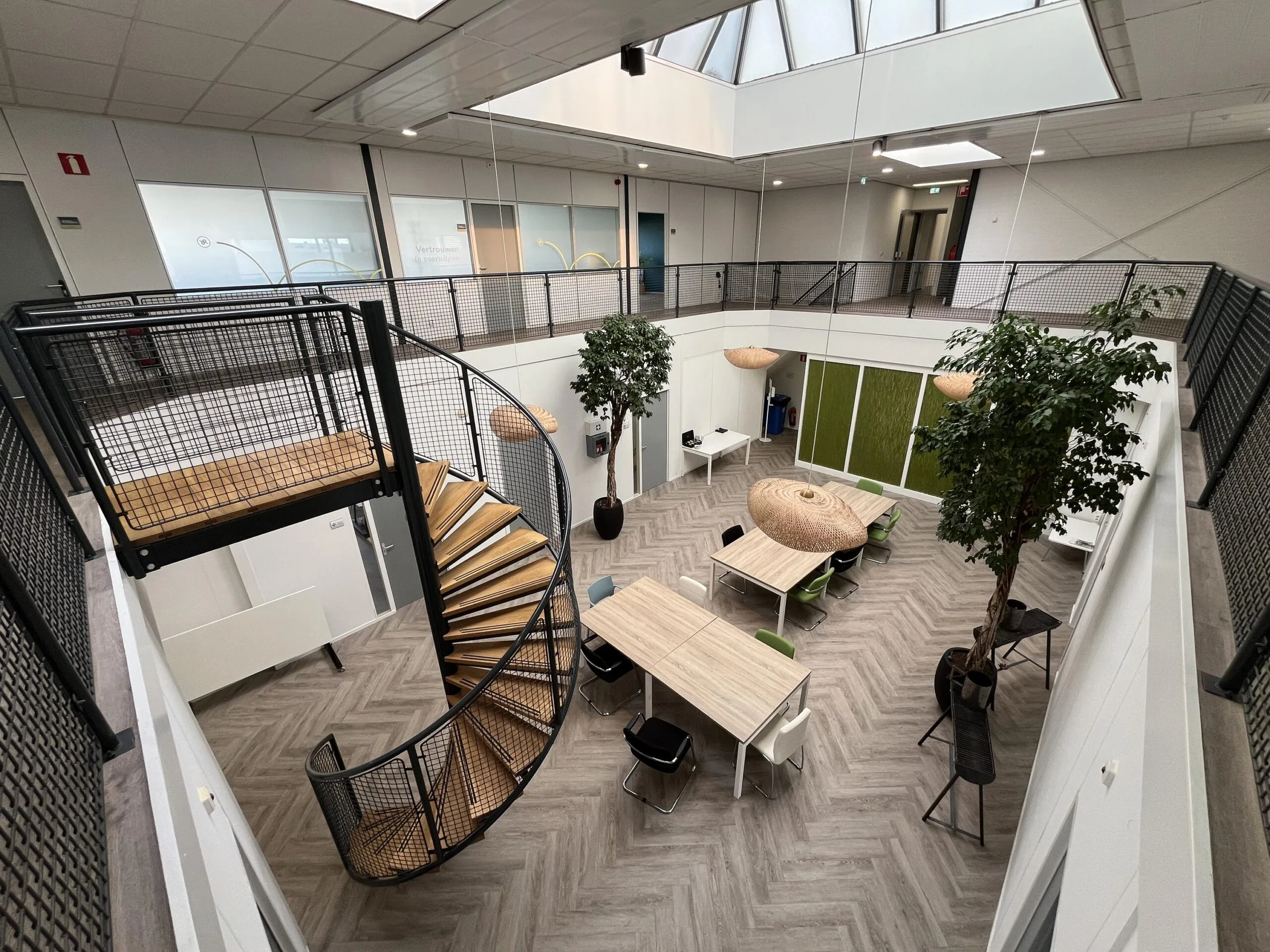 Modern office atrium on Archimedesbaan with a spiral staircase, skylight, worktables, and indoor trees.