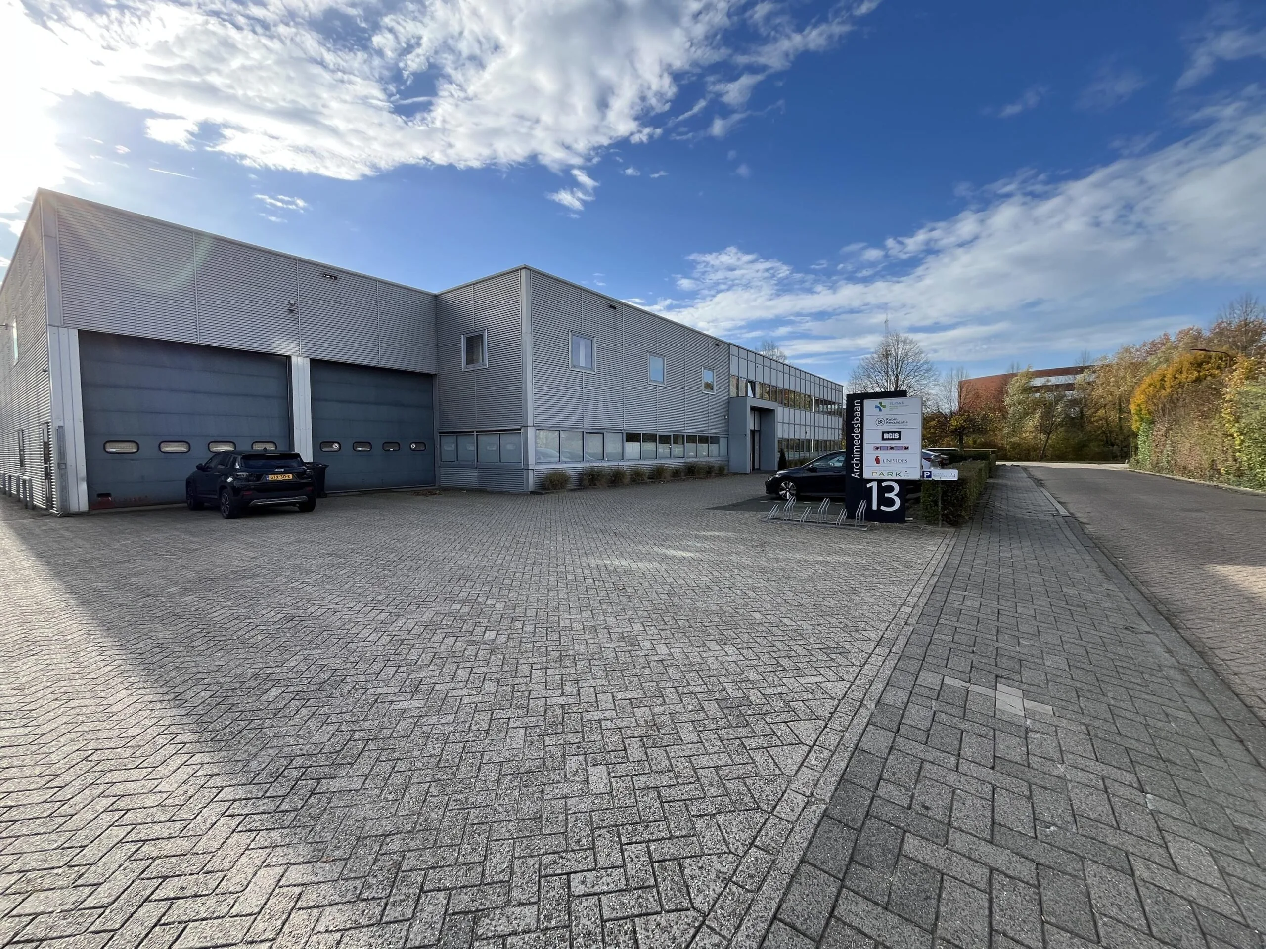 Modern industrial building with parking area at Archimedesbaan 13 under a partly cloudy sky.