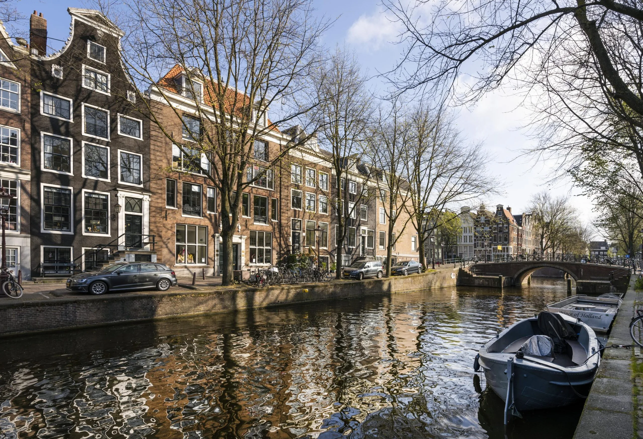 View of the Leidsegracht canal in Amsterdam with historic canal houses, parked cars, and boats along the water.