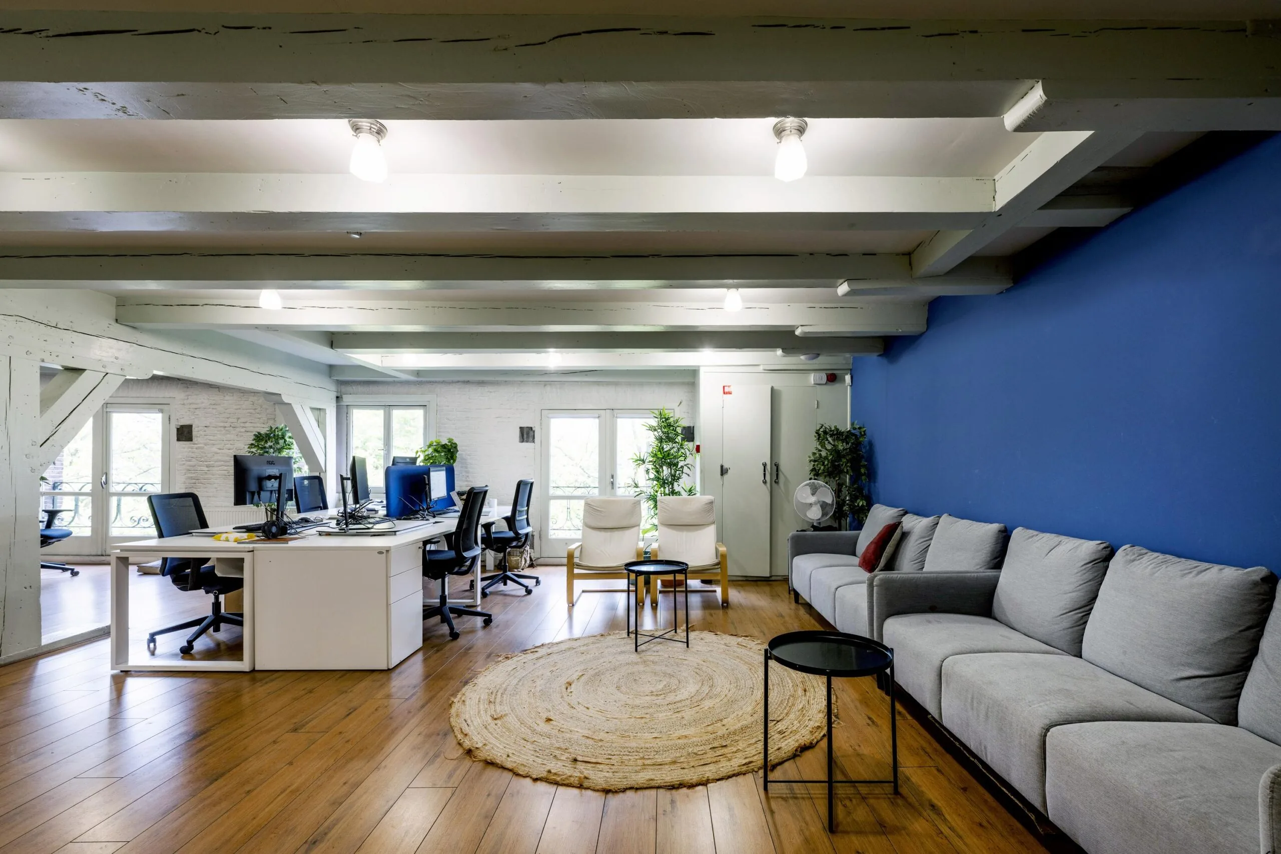 Modern open-plan office space on Leidsegracht with workstations, lounge area, and a vibrant blue accent wall.