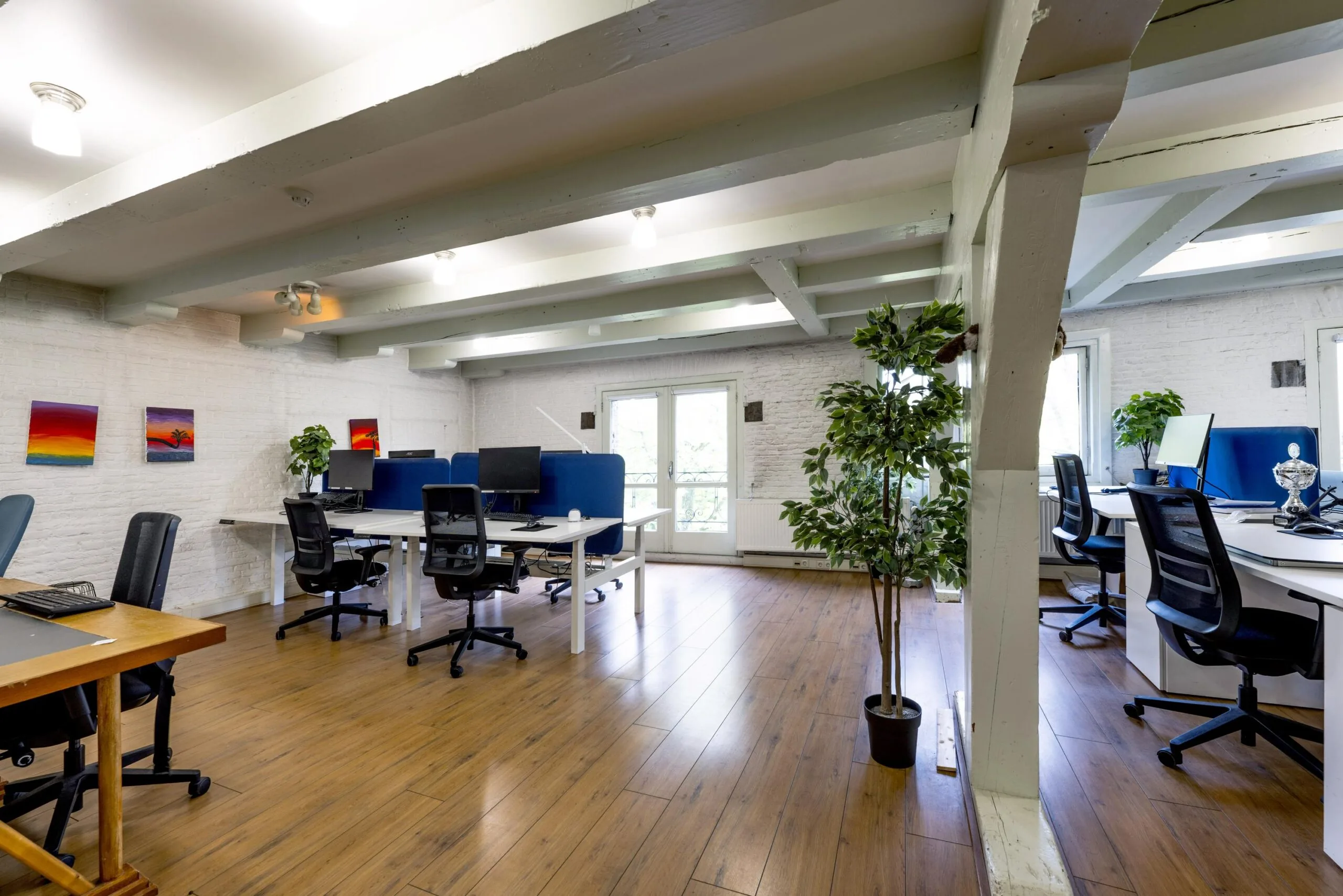 Modern open-plan office space on Leidsegracht with wooden floors, white beams, and desk workstations.