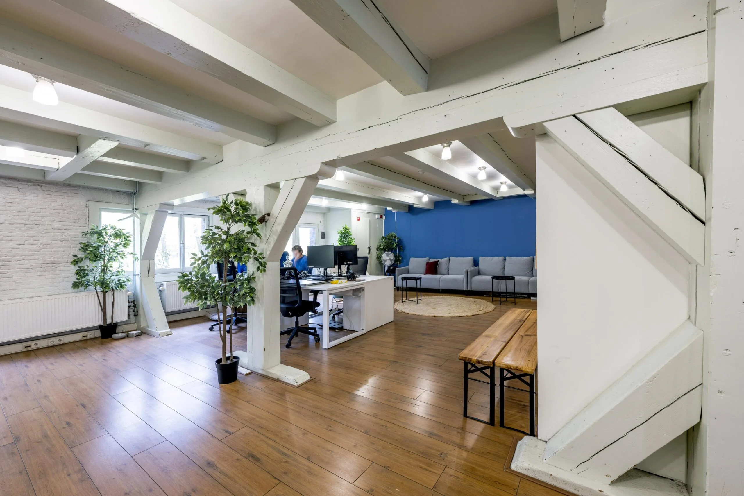 Modern office space on Leidsegracht with wooden floors, exposed beams, and a mix of desks, seating area, and indoor plants.