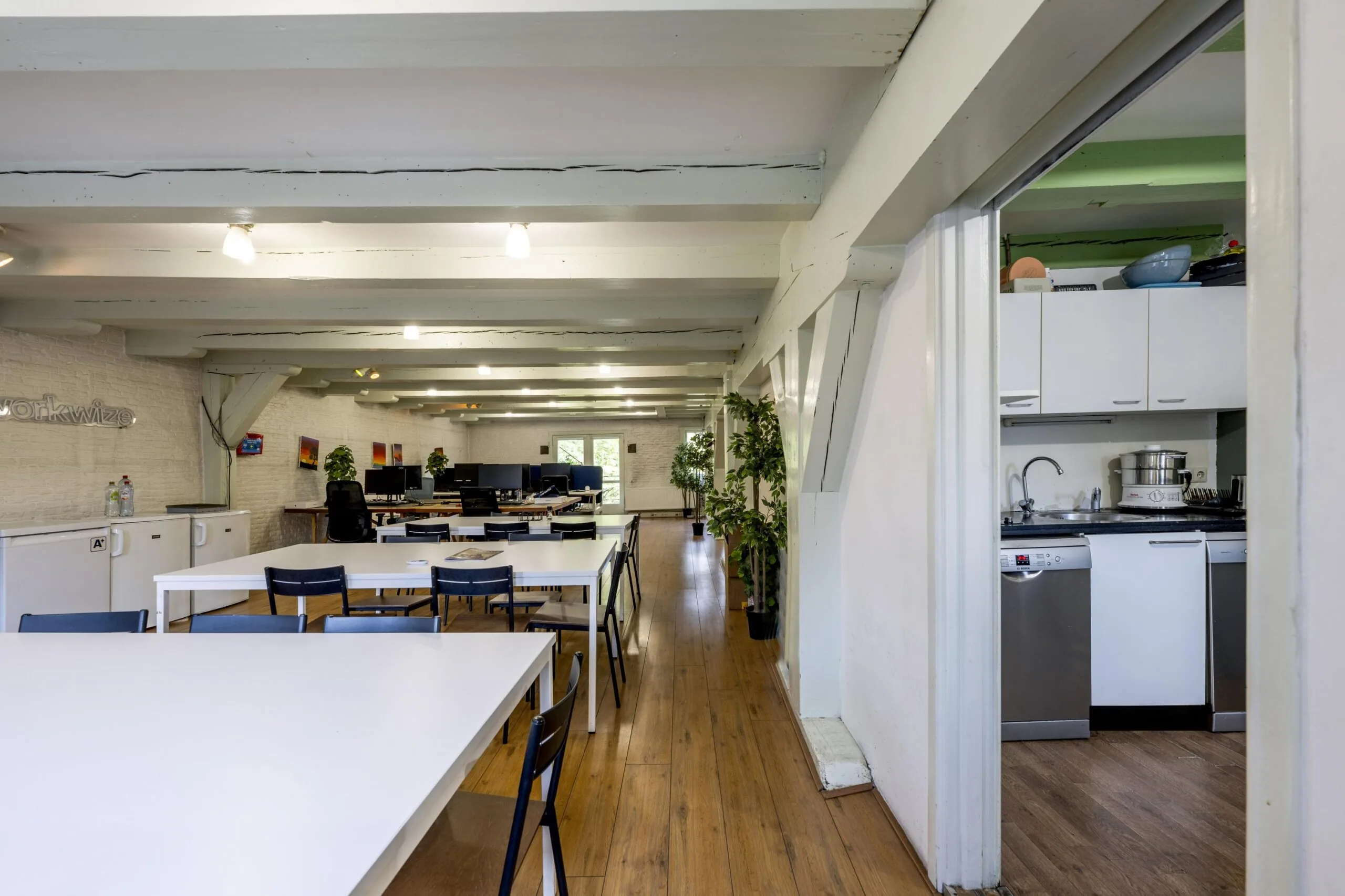 Modern coworking space on Leidsegracht with white desks, wooden flooring, and an adjacent kitchen area.