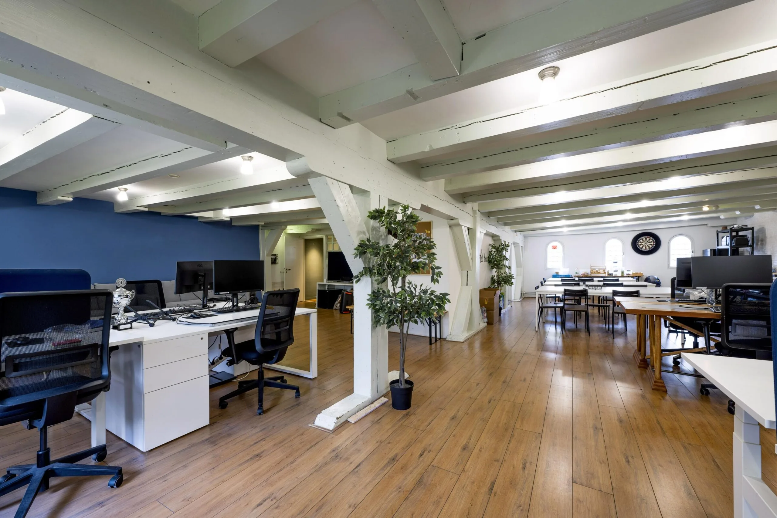 Modern open-plan office space on Leidsegracht with wooden floors, white beams, desks, and natural lighting.