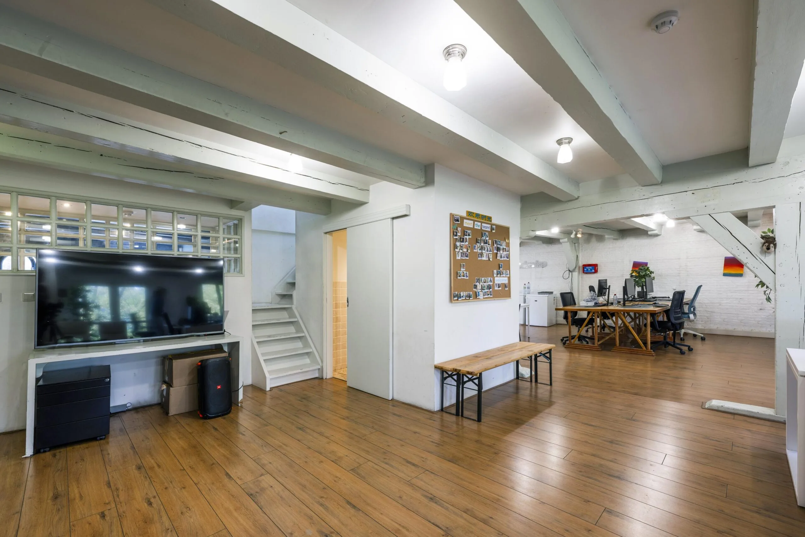 Modern office space on Leidsegracht with wooden flooring, exposed beams, a large TV, desk area, and a photo-covered bulletin board.