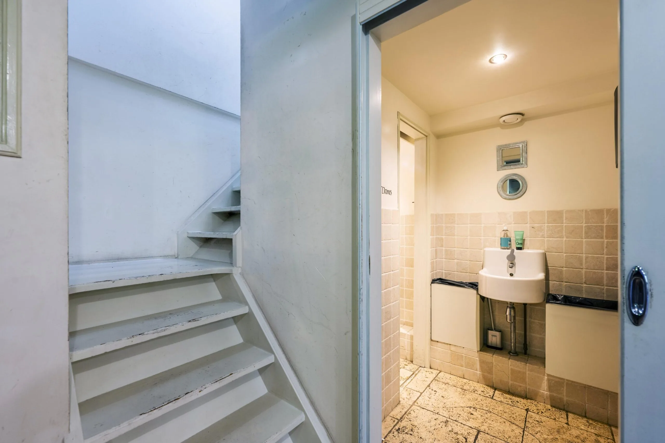 Small tiled bathroom with a white sink and decorative mirrors, next to a narrow staircase in a building on Leidsegracht.
